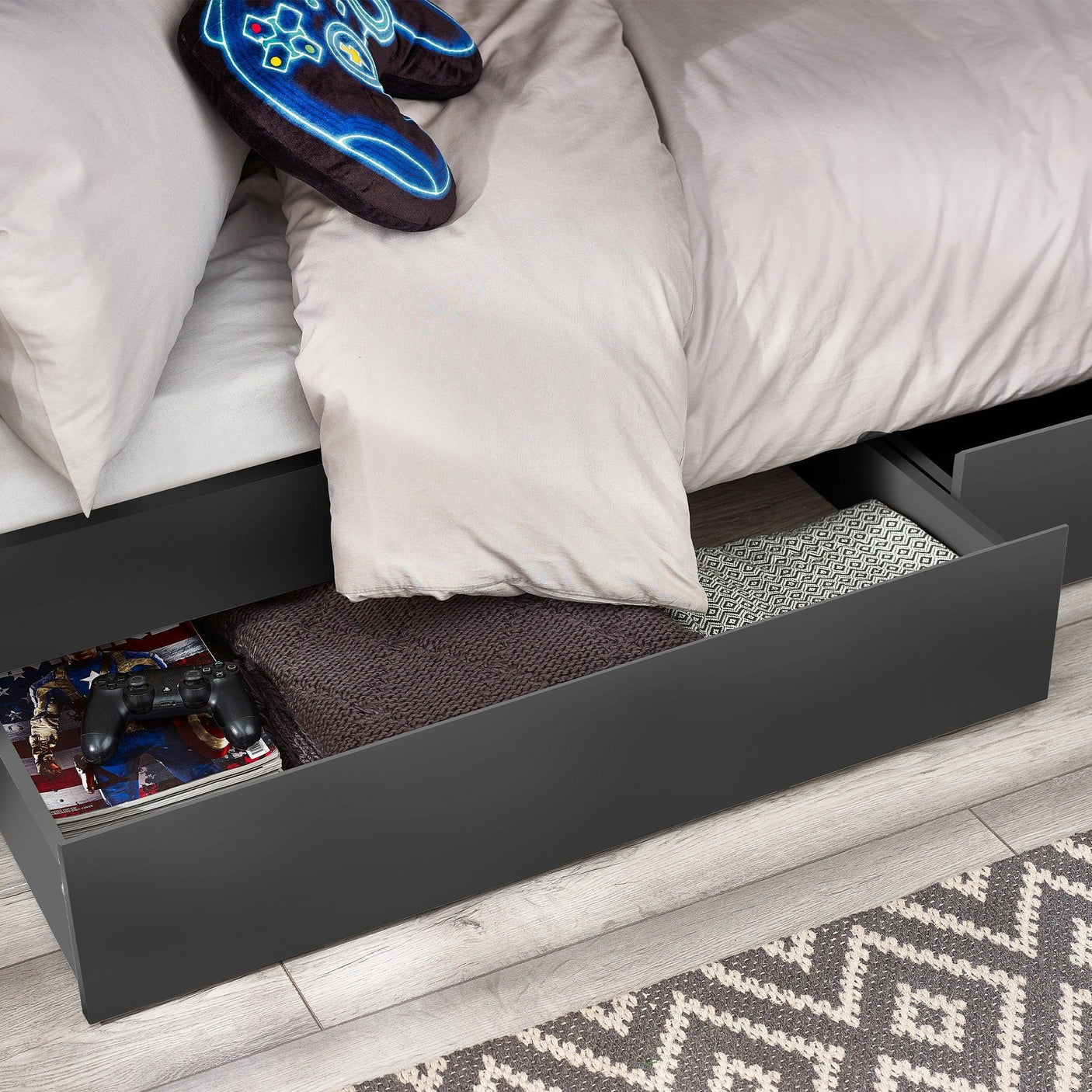 Anthracite bunk bed storage drawer open with blanket, controller, books and patterned rug visible
