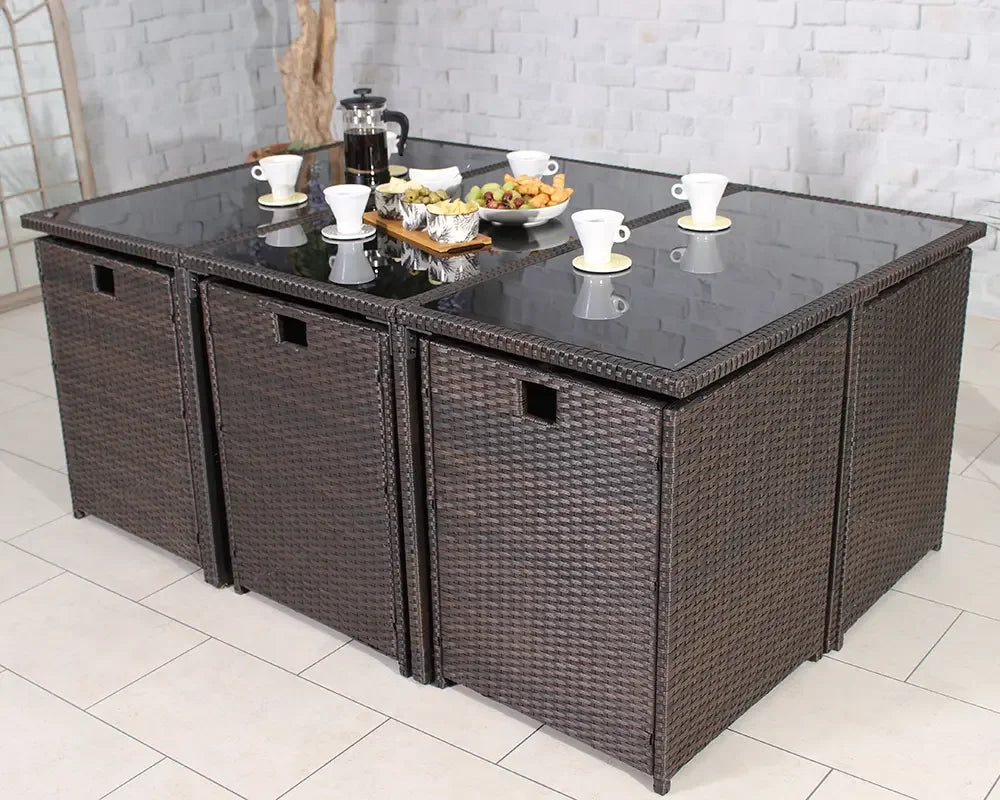 Brown rattan garden dining set with glass top table and matching cube chairs arranged indoors
