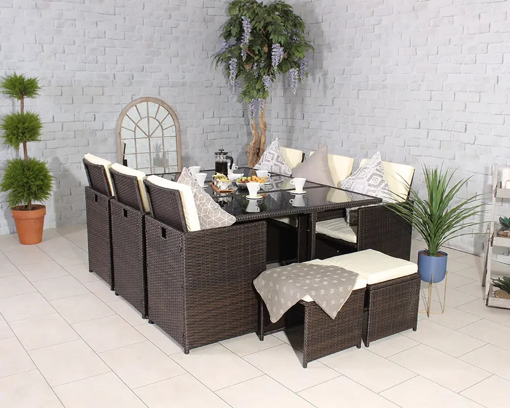 Brown rattan dining set with glass table, cream cushions, and stools in a tiled room
