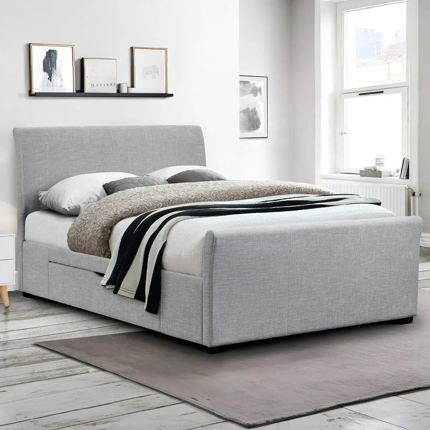 Light grey upholstered double bed with storage in modern bedroom with artwork and window