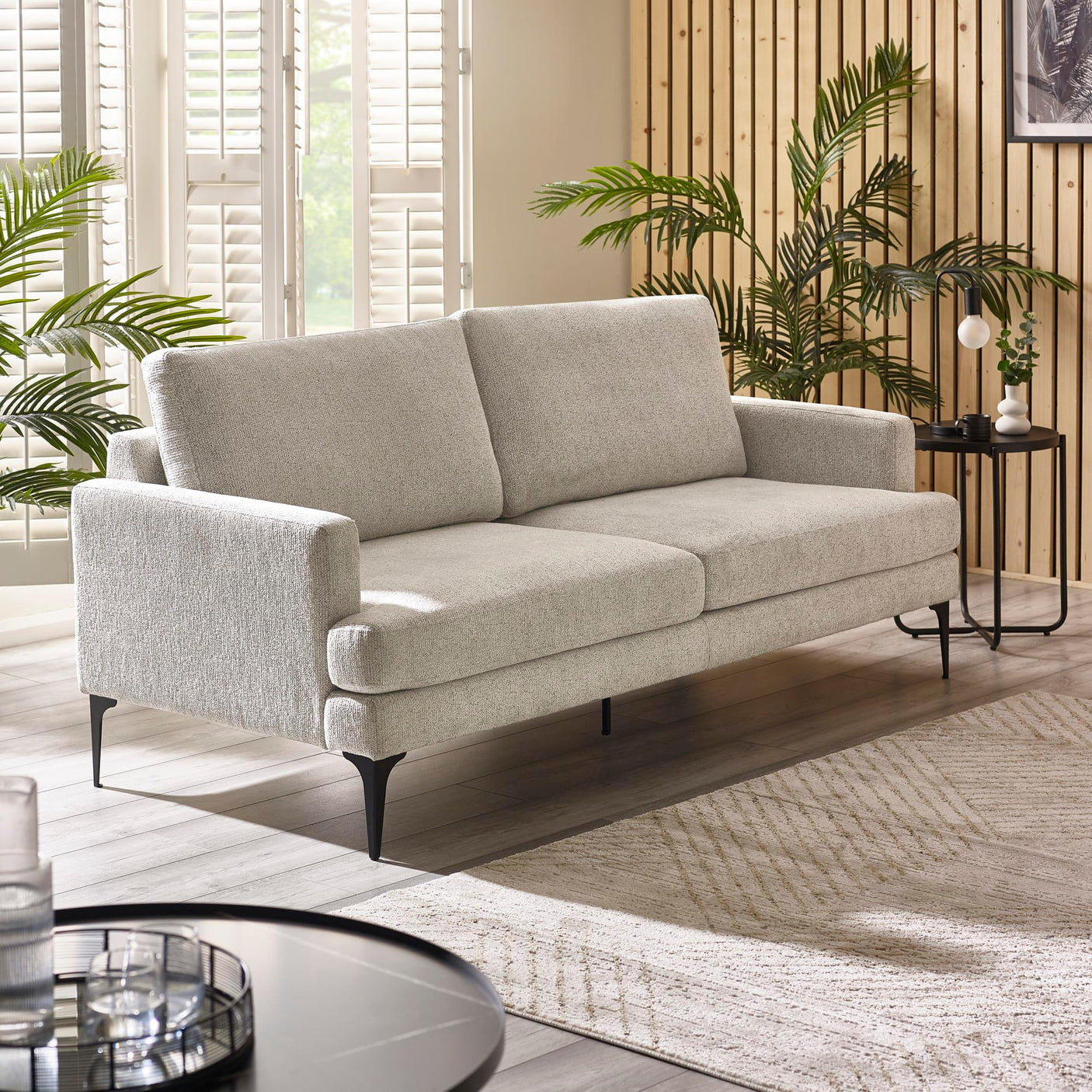 Light grey fabric sofa with black legs in a modern living room with wood panel wall