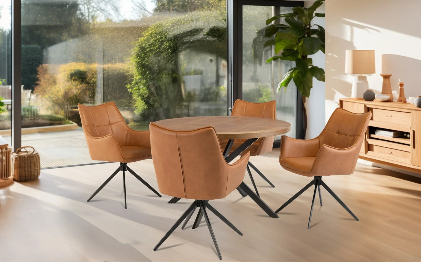 Round wood dining table with four tan leather chairs on black metal legs in modern room