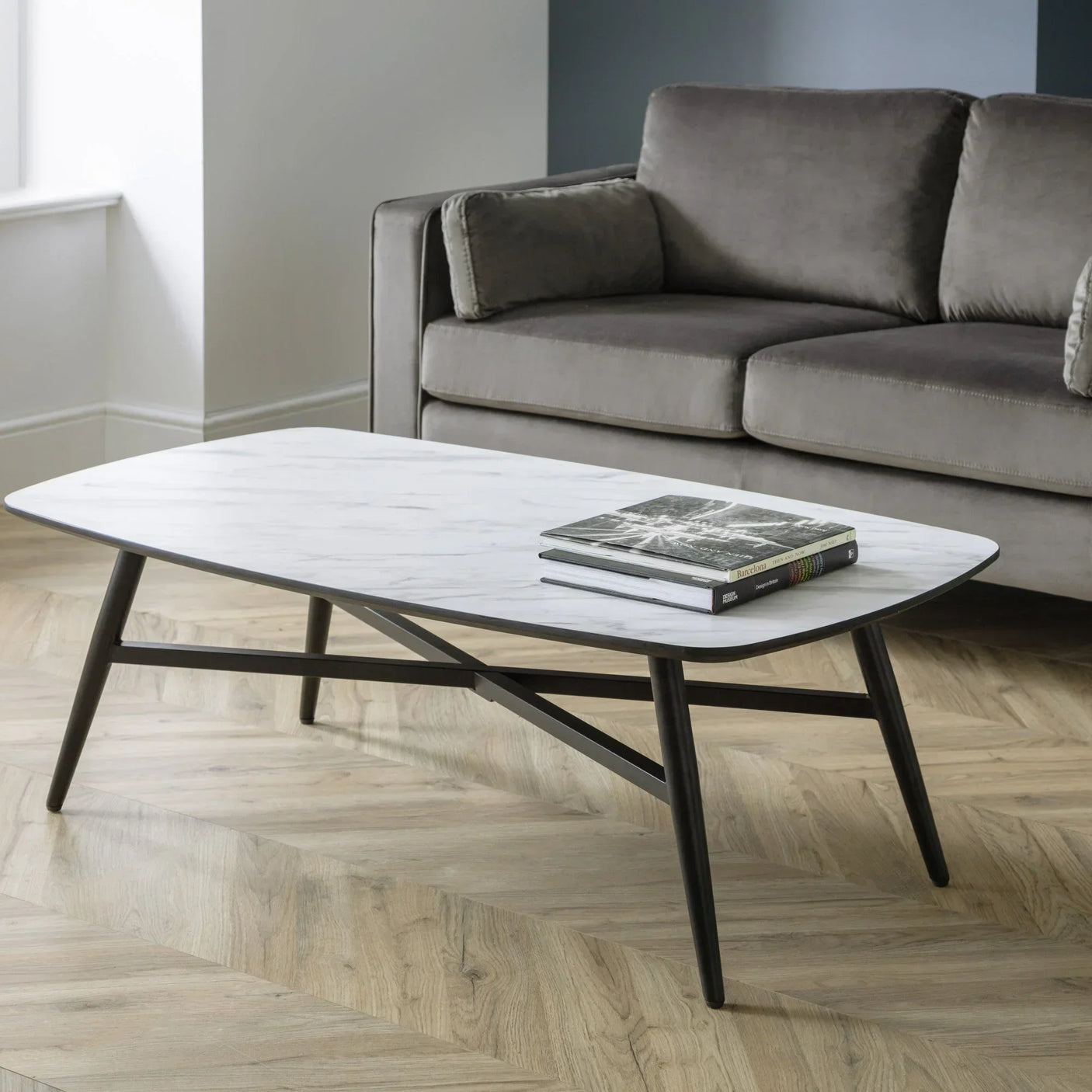 Modern marble coffee table with black legs beside a grey sofa on wooden flooring