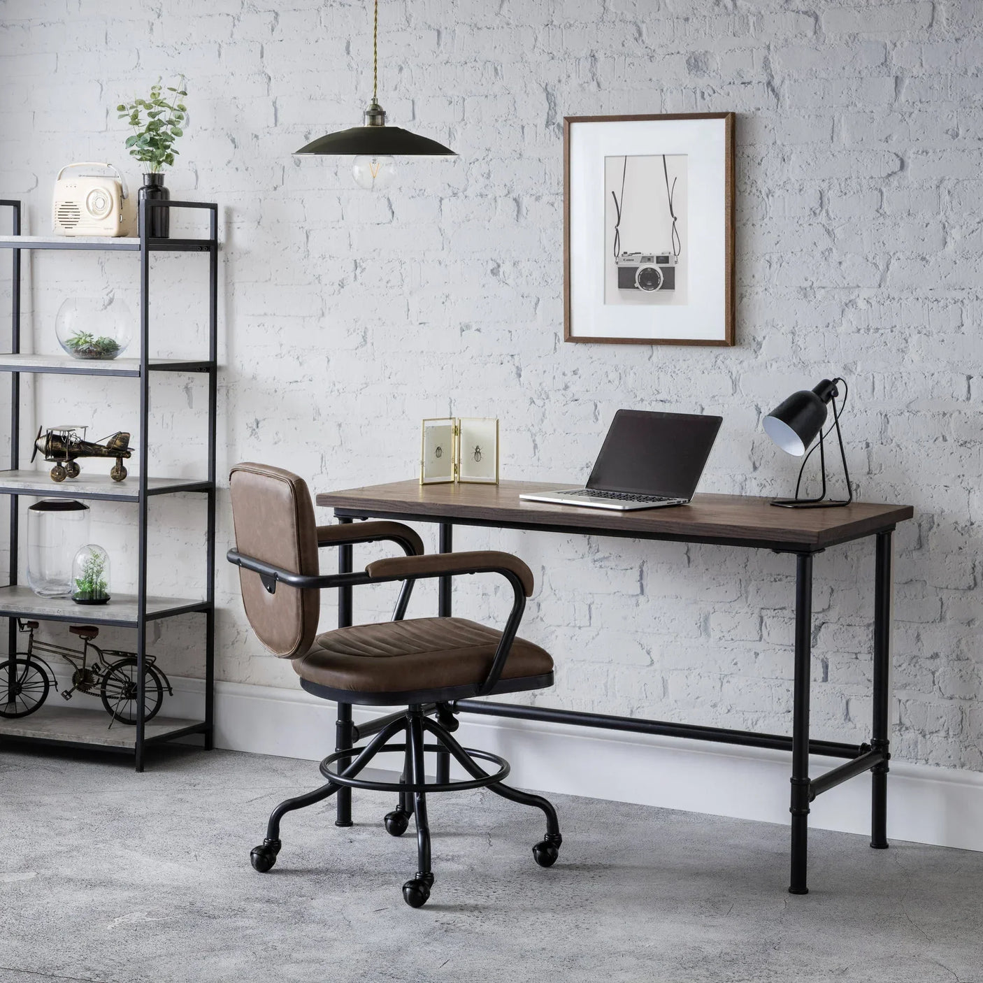 Industrial pipe desk with dark wood top and office chair against white brick wall