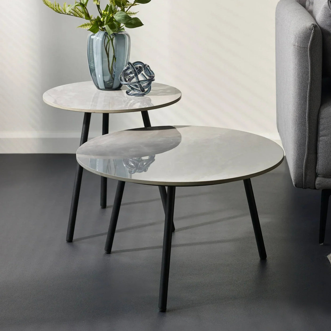 Round marble top nesting tables with black legs beside grey sofa