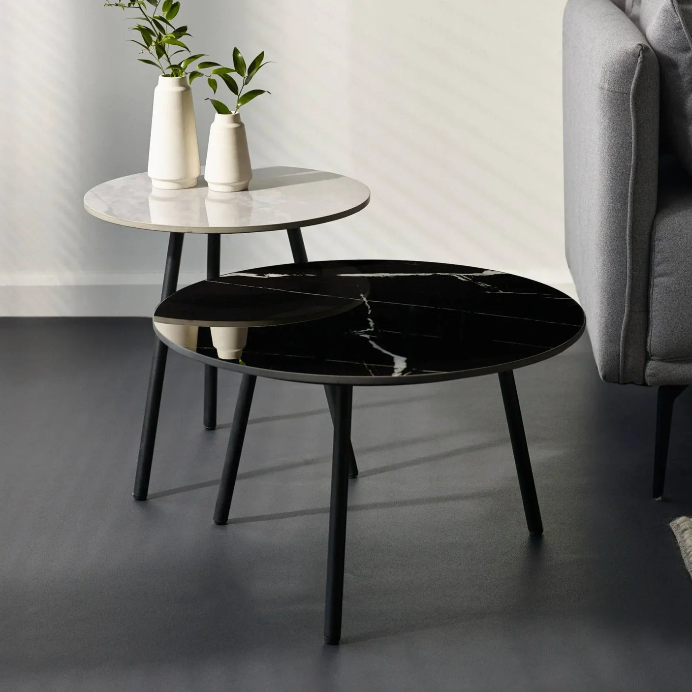 Round black and white marble coffee tables with slim legs beside grey sofa