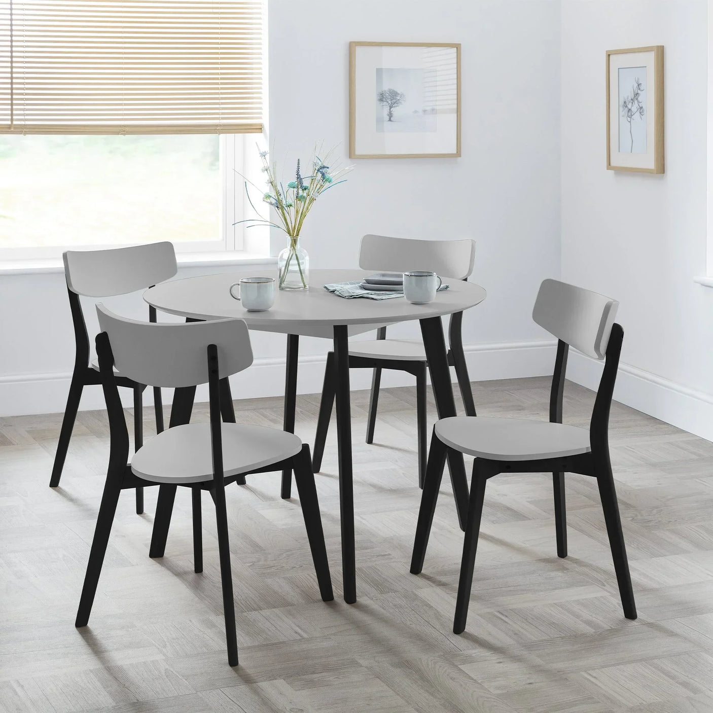 Grey round dining table set with four black leg chairs in bright modern room