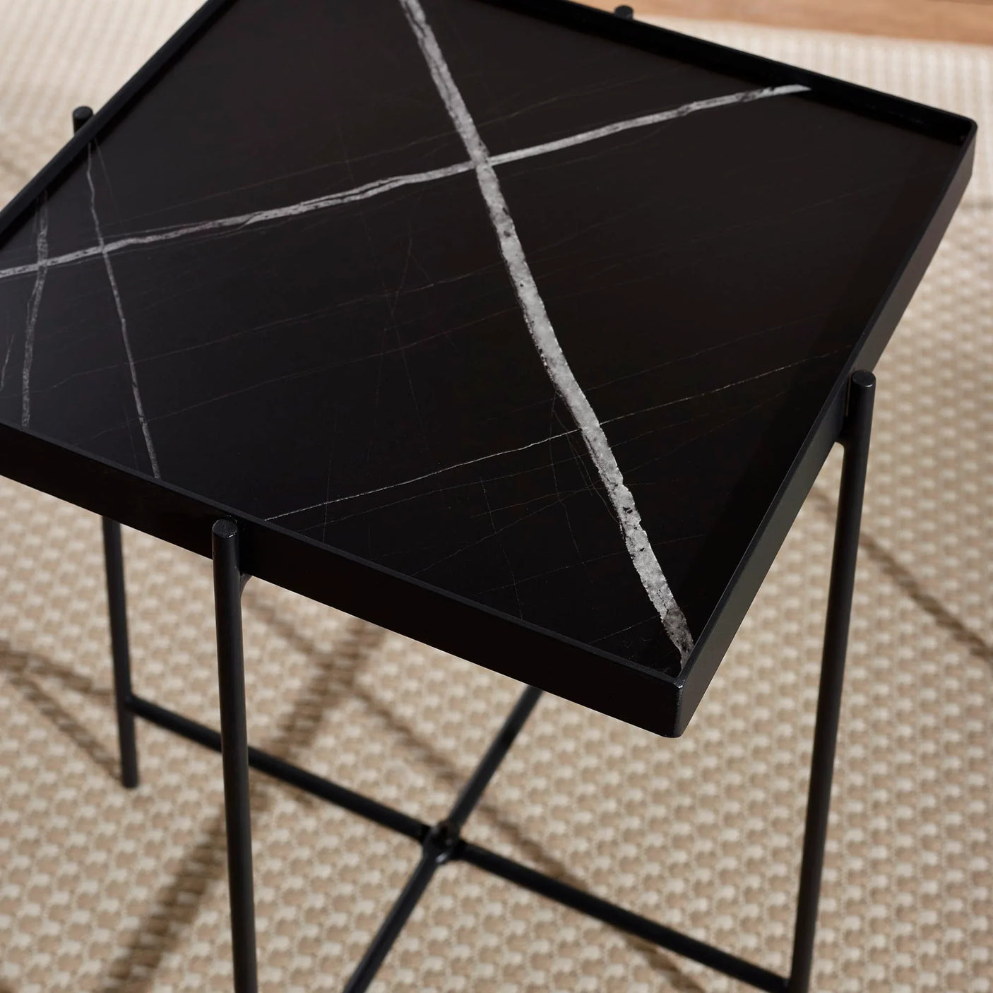 Black marble side table with white veining and slim metal legs on beige patterned rug