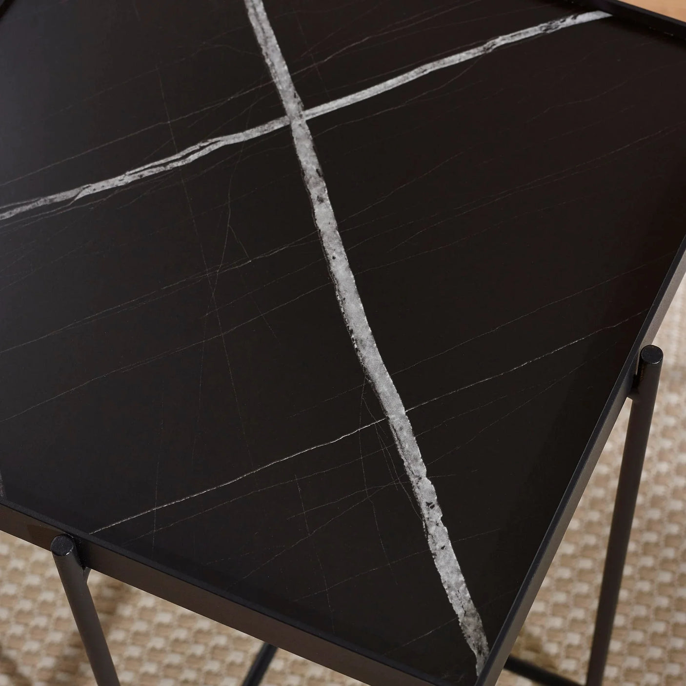 Black marble side table with white veining and metal legs on textured carpet