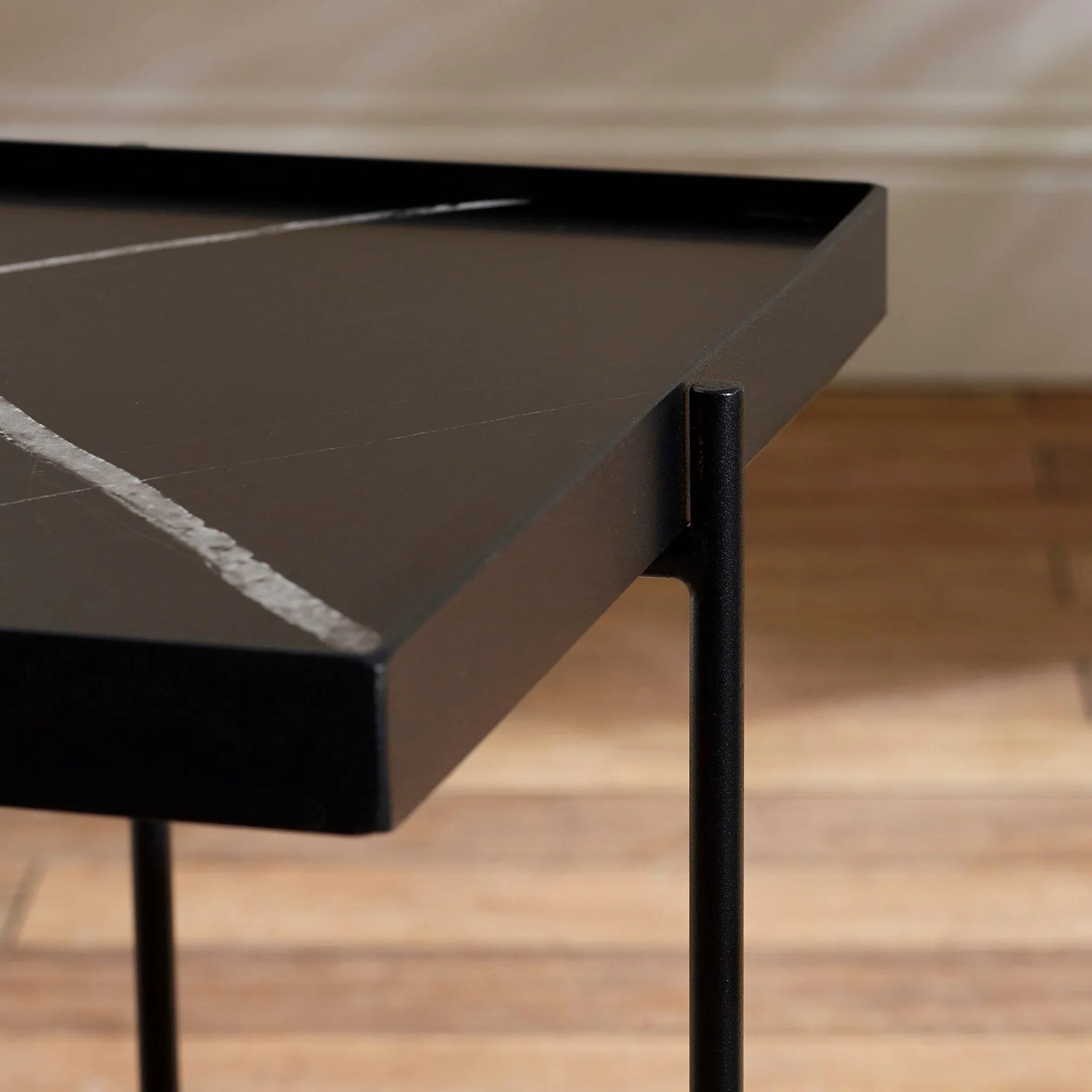 Black marble side table with metal legs and white veining, close-up of corner detail