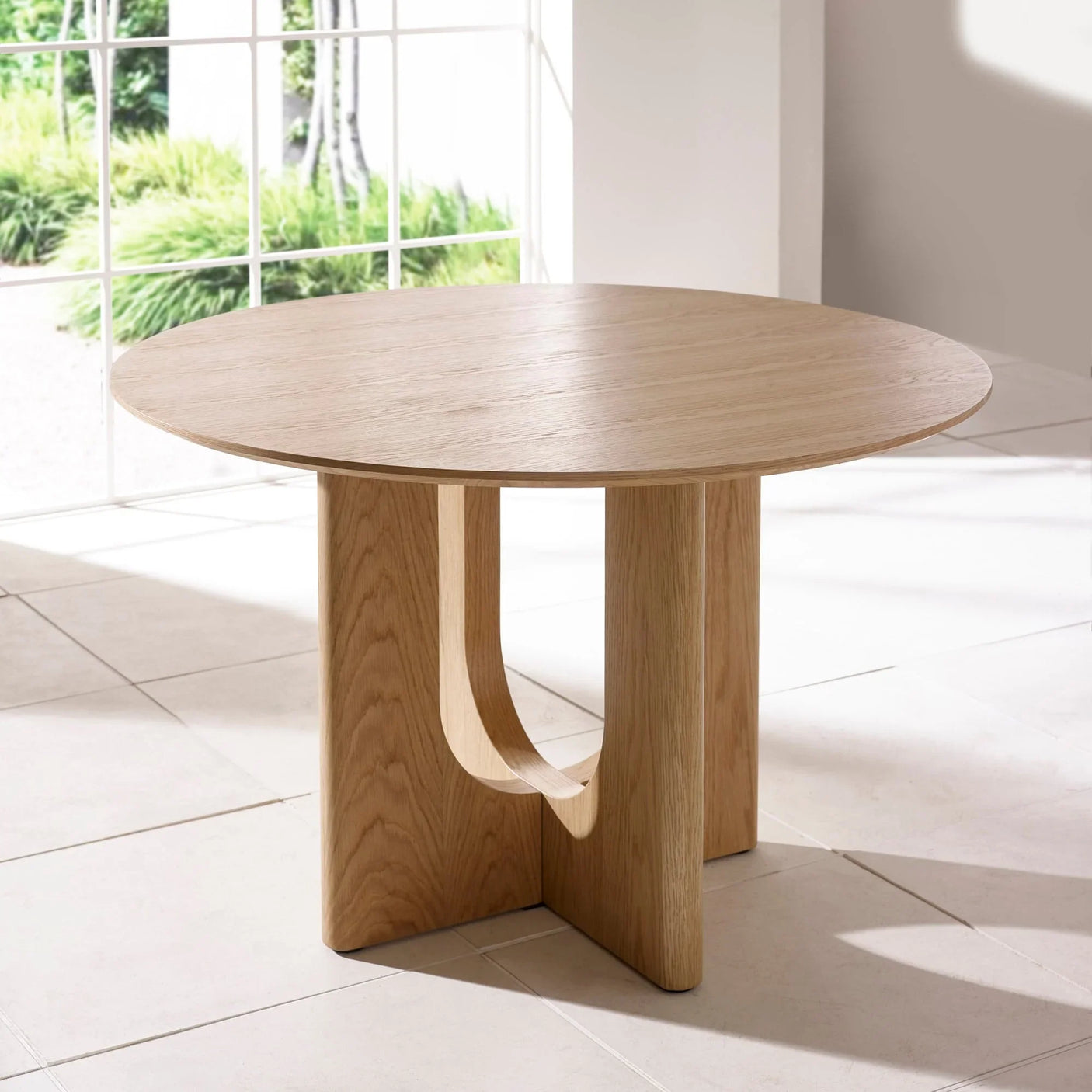 Round oak dining table with curved pedestal base on tiled floor in bright room