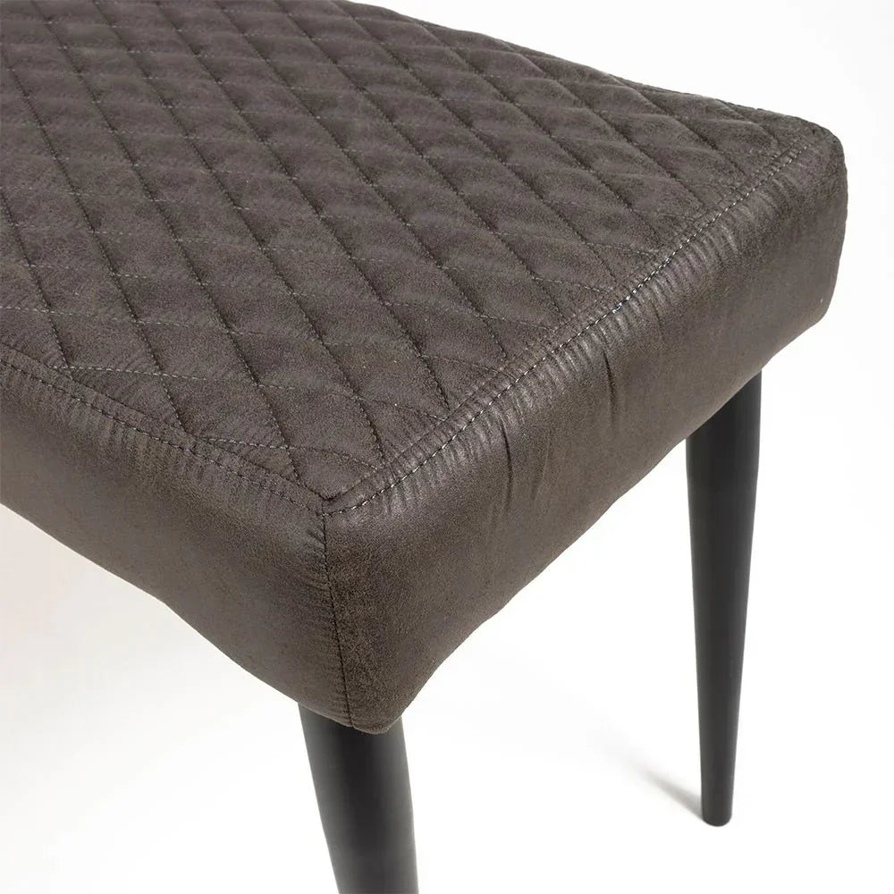 Closeup of grey dining chair seat with quilted upholstery and black tapered legs