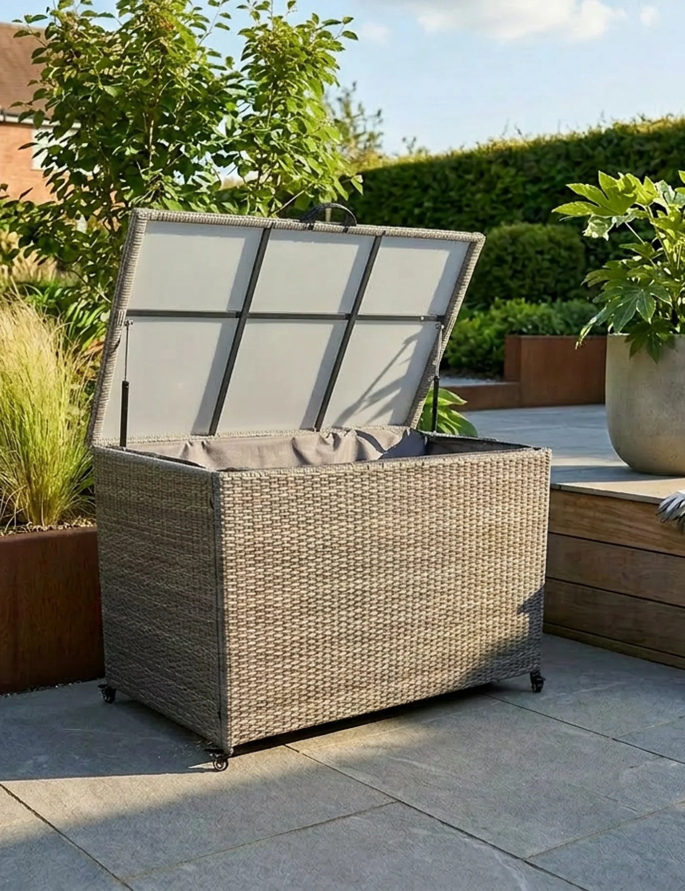 Rattan outdoor storage box with open lid on a patio surrounded by plants