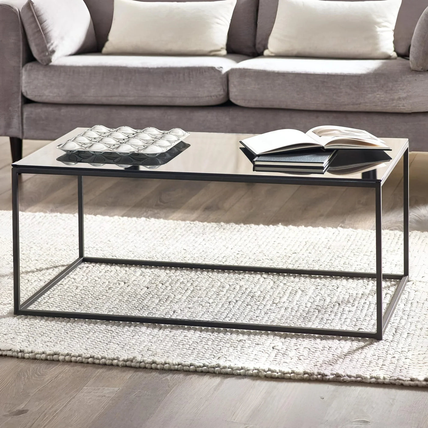 Glass top coffee table with black metal frame on textured rug in modern living room