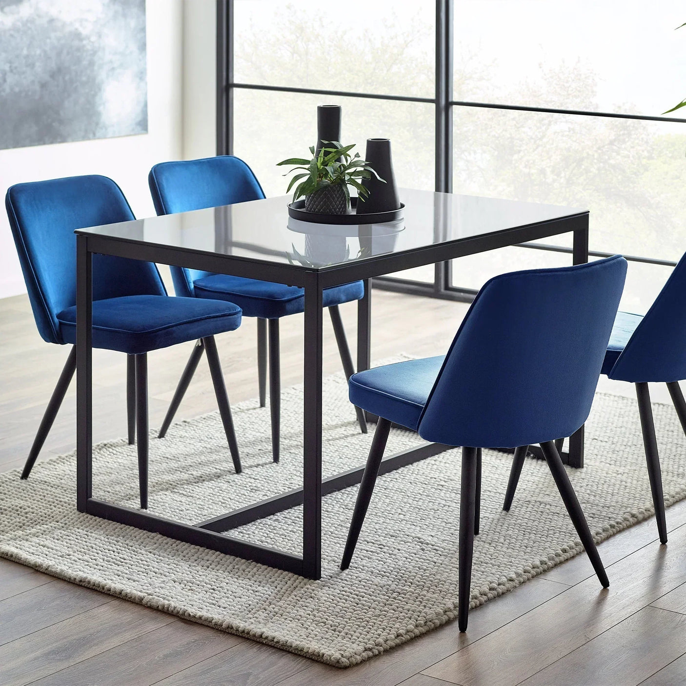 Glass dining table with blue velvet chairs on a textured rug in modern dining room