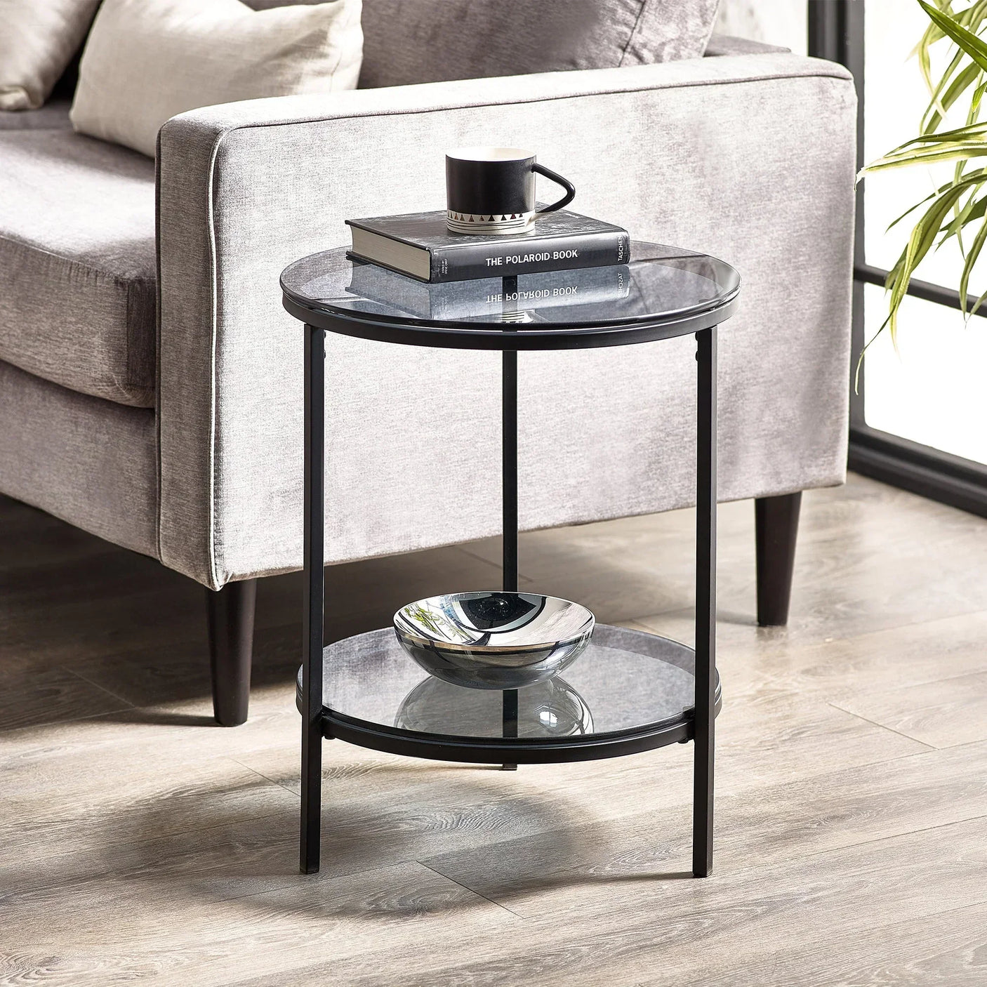 Round glass lamp table with black metal frame beside grey sofa on wooden floor