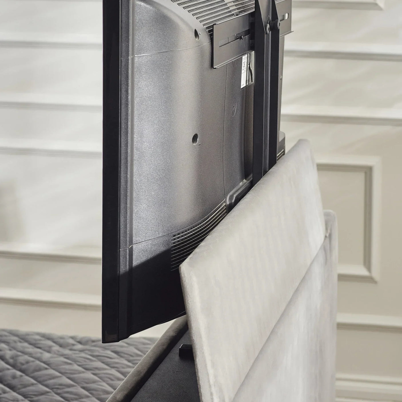 Side view of TV lift bed mechanism with grey upholstered headboard and mounted television