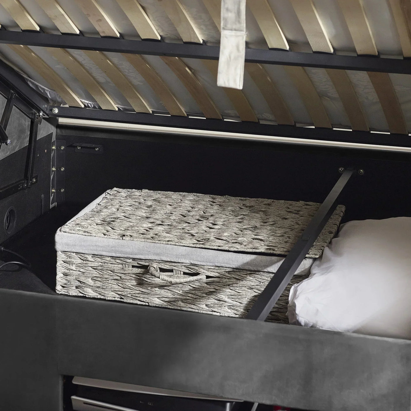 Ottoman storage bed open with grey wicker basket and pillow inside storage compartment