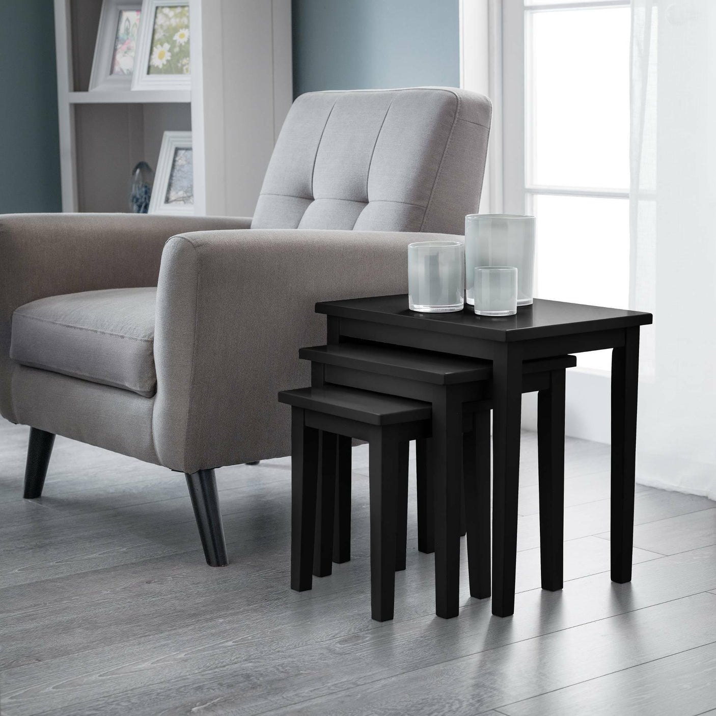 Black nest of tables with candles beside a grey armchair in a modern living room