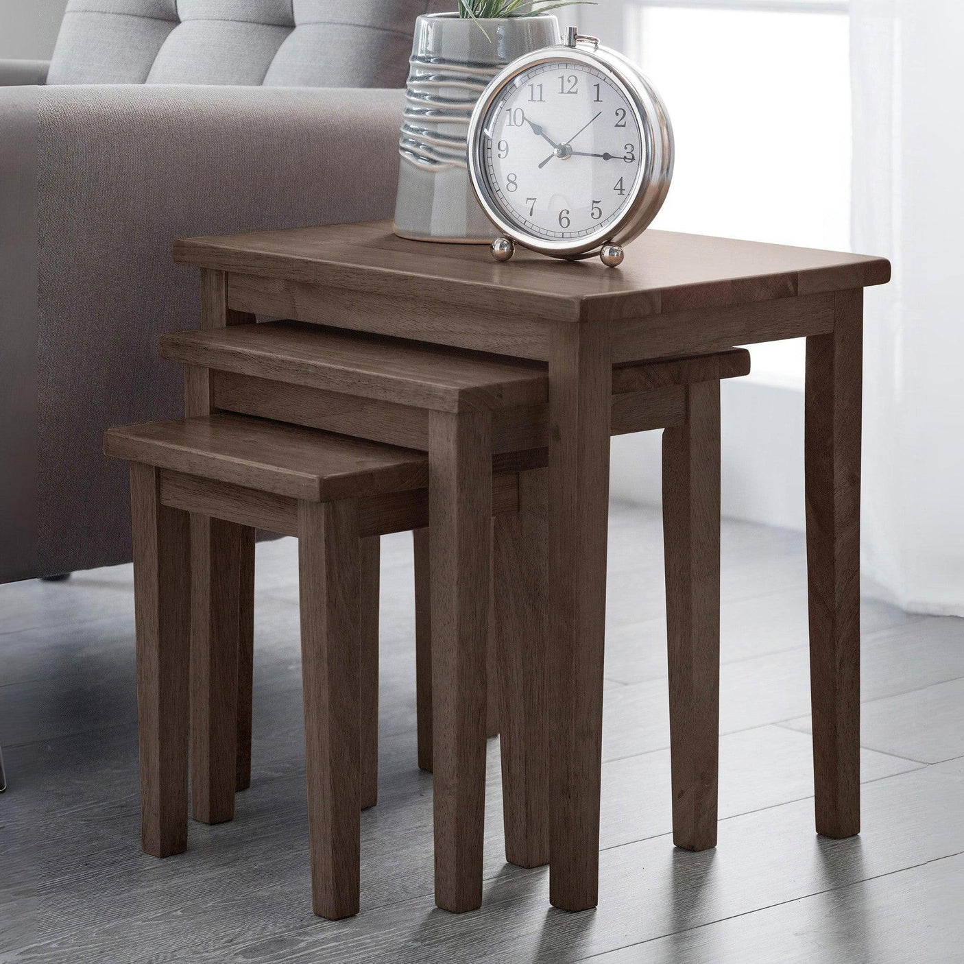 Walnut nest of tables set in living room with clock and vase on top