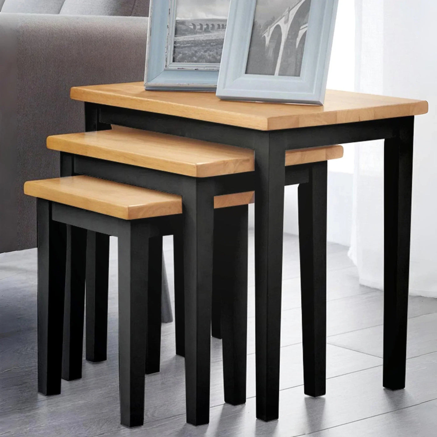Set of three nesting tables with black legs and light oak tops in living room corner