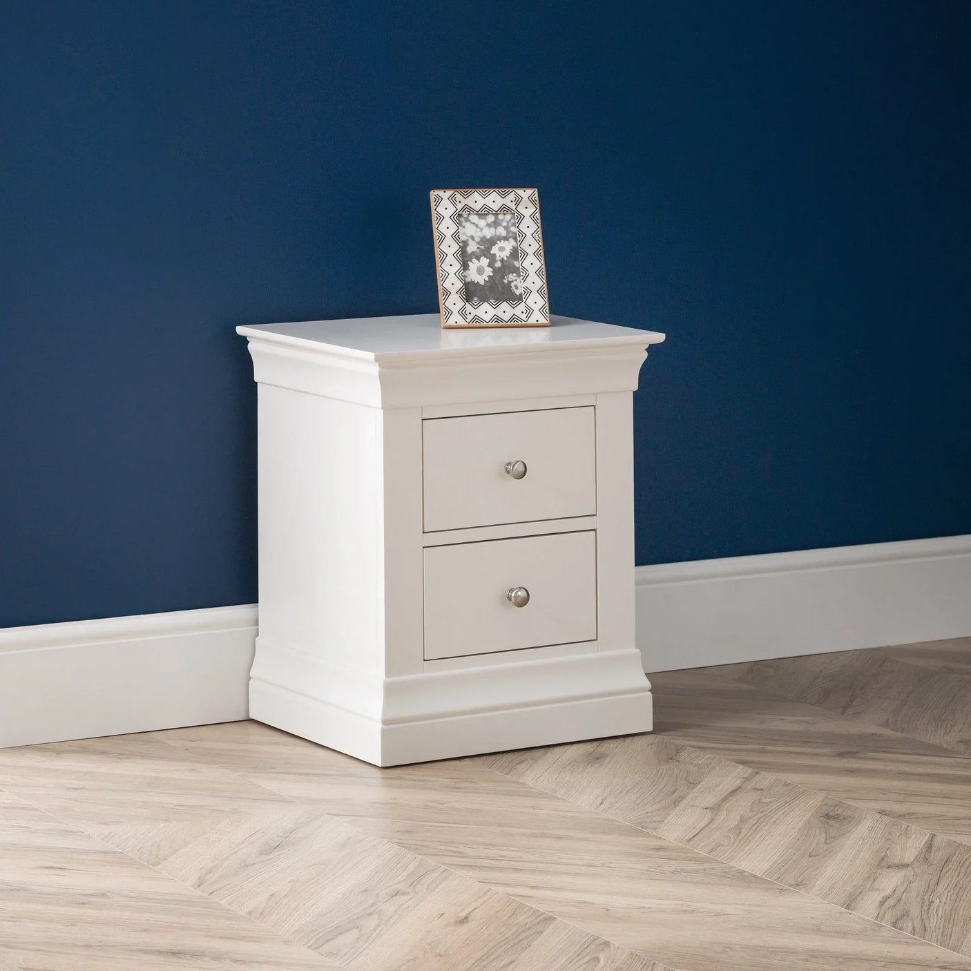 White two drawer bedside table with photo frame against blue wall on wood flooring