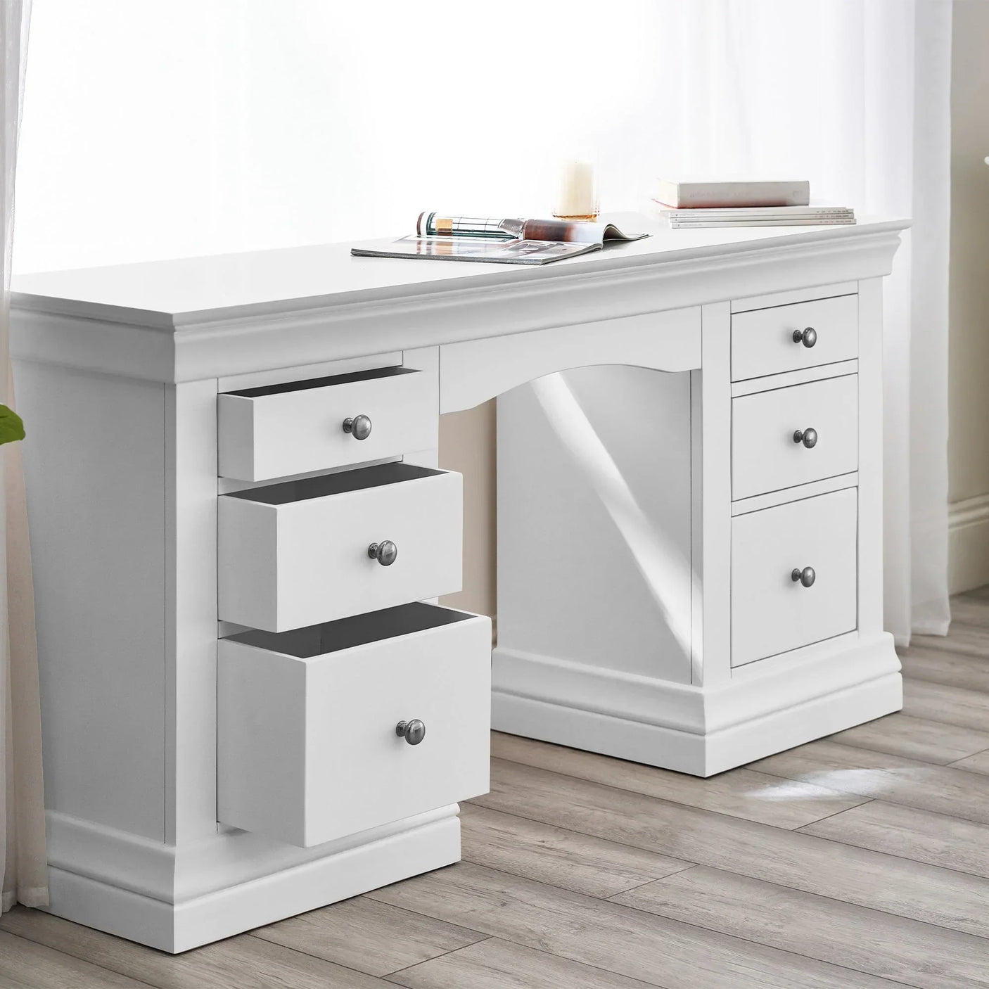 White dressing table with six drawers and silver handles in a bright room with wood flooring
