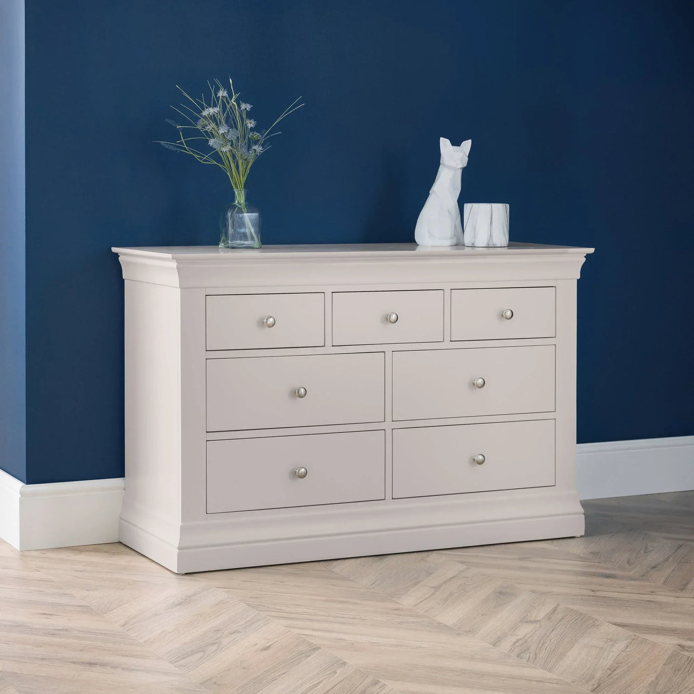 Light grey 7 drawer chest in modern room with blue wall, decorative vase and figurine on top