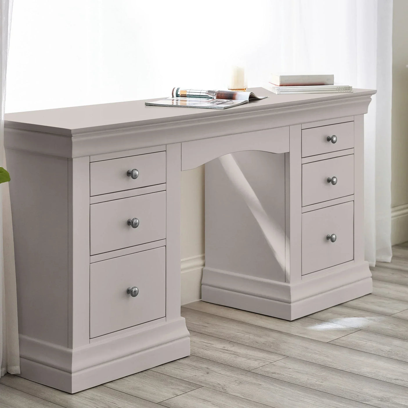 Grey dressing table with six drawers and silver handles in bright room with wood flooring
