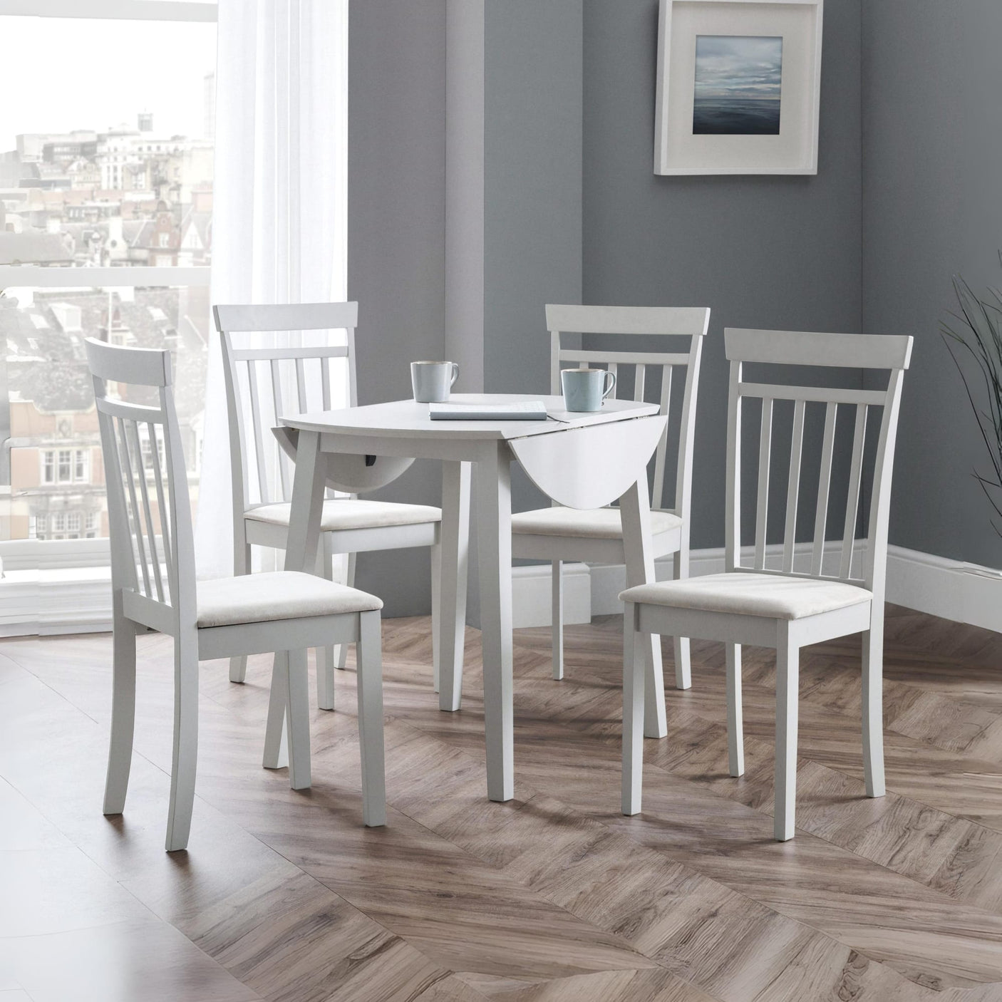 White round Coast dropleaf table with one leaf dropped, three white chairs in bright room with wood floor
