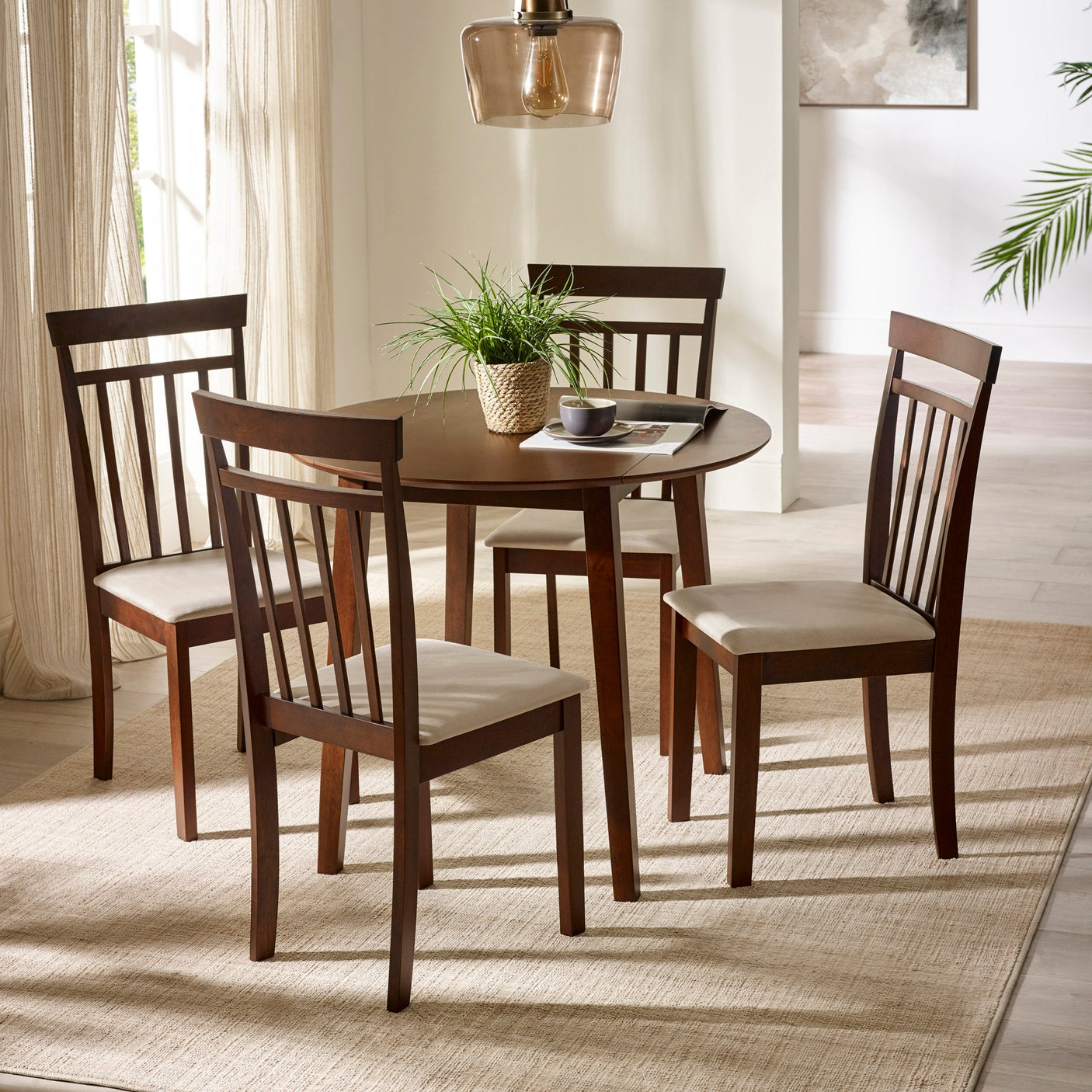 Two dark wood chairs with beige cushions with round dark wood dining table under glass pendant in bright room