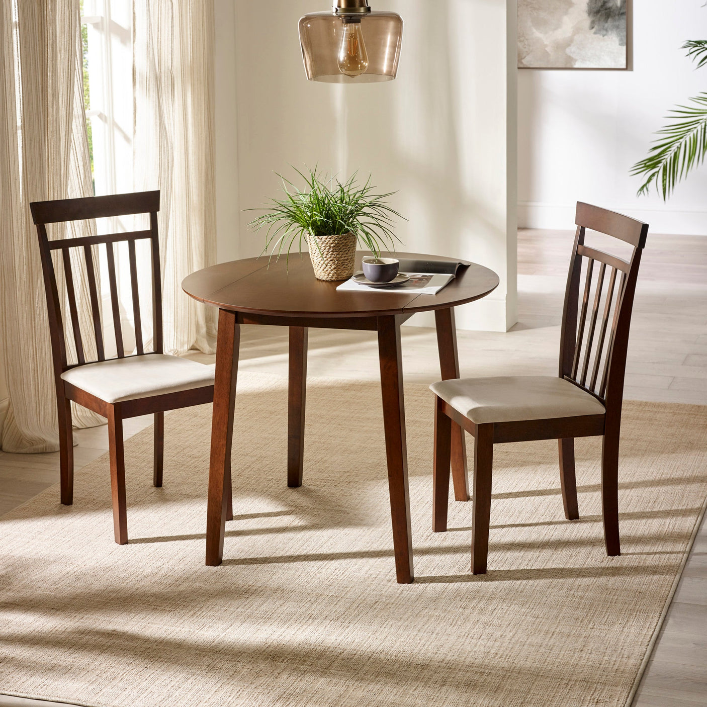Round dark wood dining table with two matching chairs with beige cushions in bright room with rug