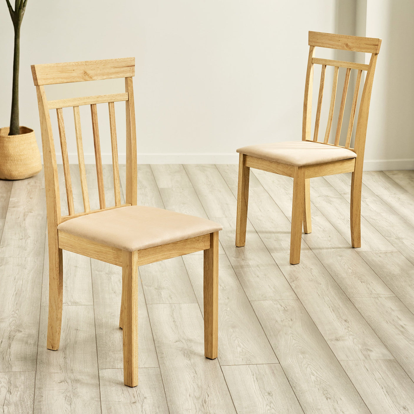 Two light wood dining chairs with beige cushions positioned on gray wood floor in bright room