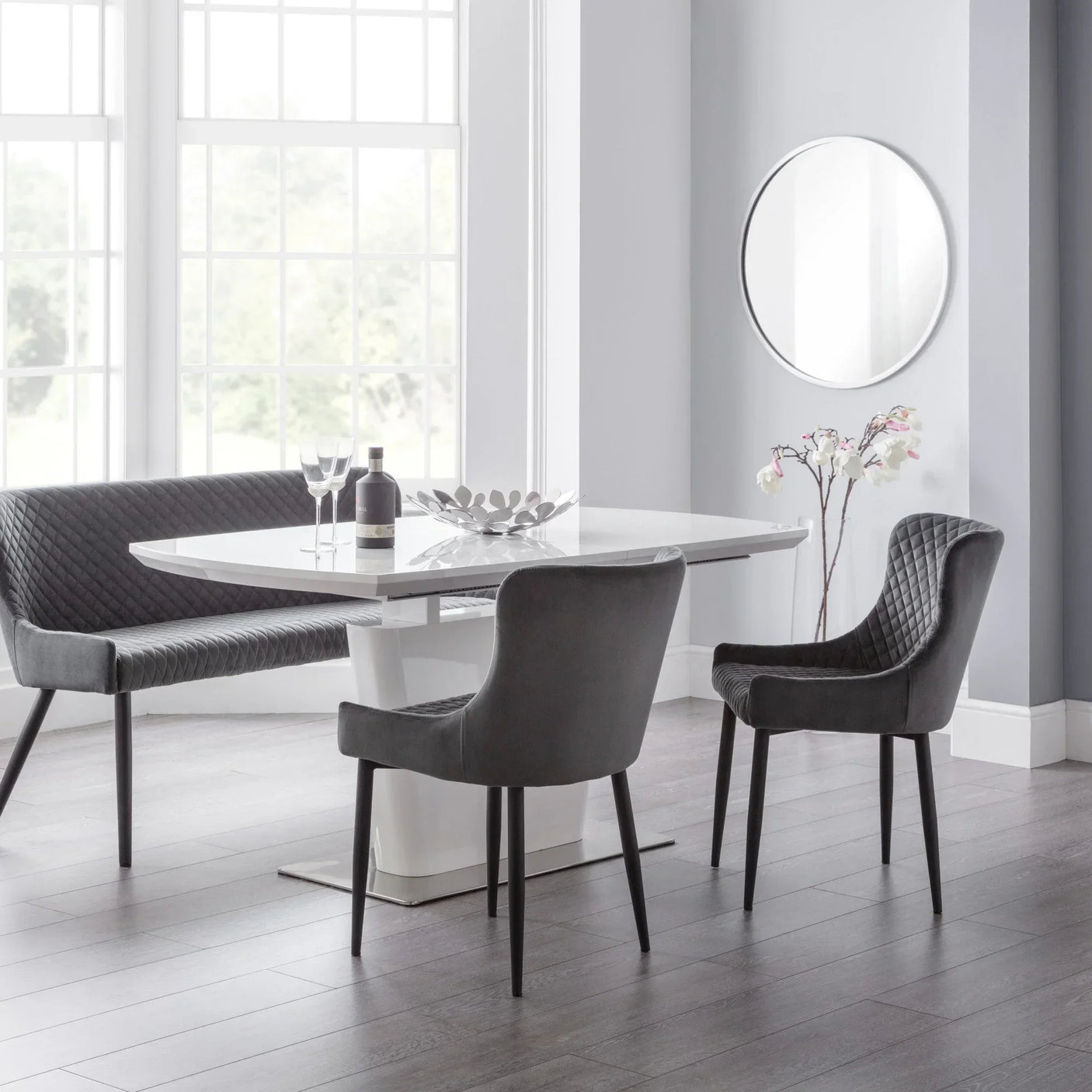 Grey velvet dining chairs and bench with quilted back around white rectangular dining table