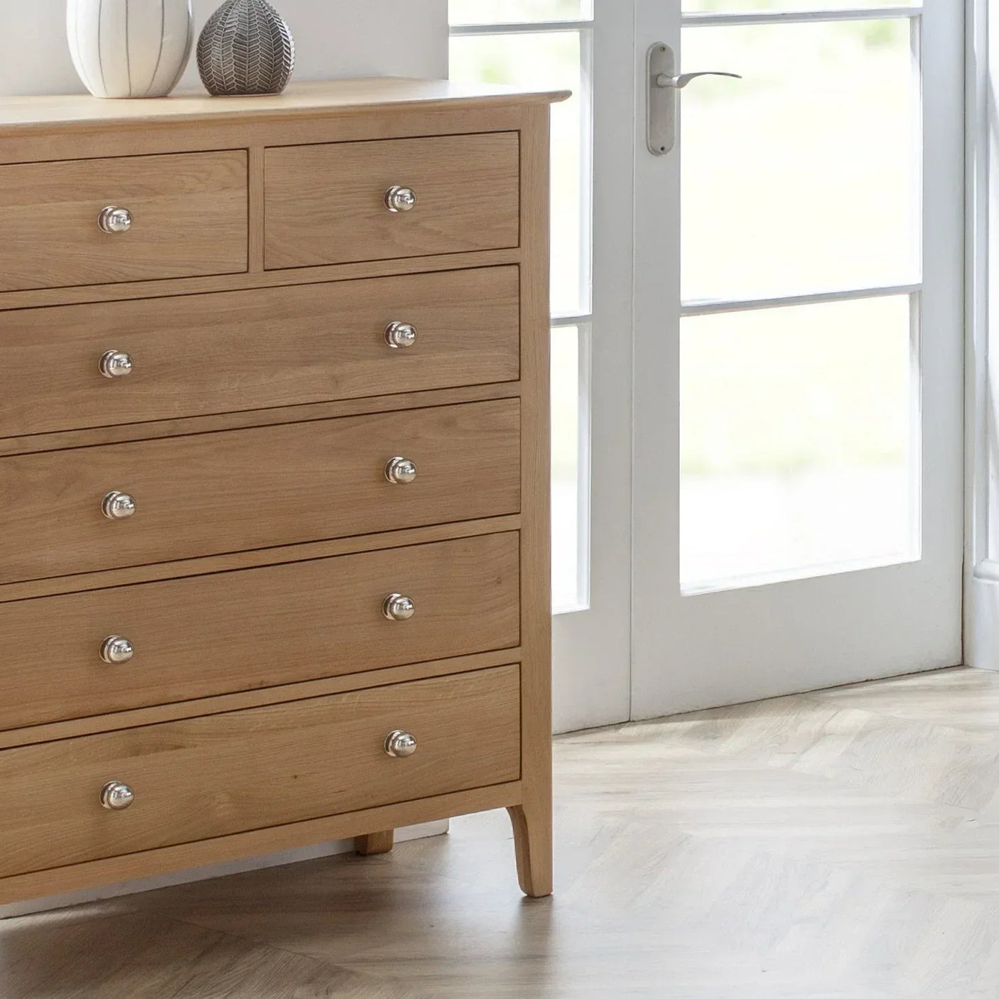 Oak 4+2 drawer chest with silver handles beside glass doors in bright room