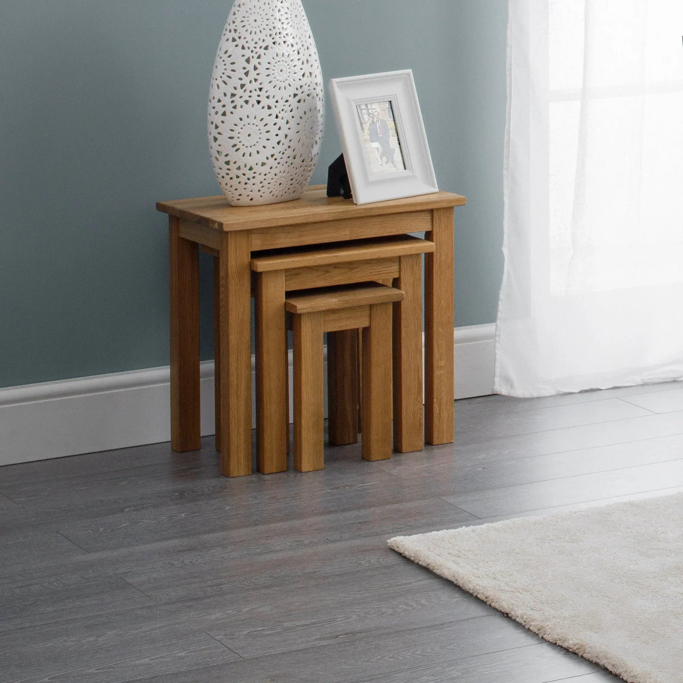 Oak nest of tables set with decorative vase and photo frame in modern living room