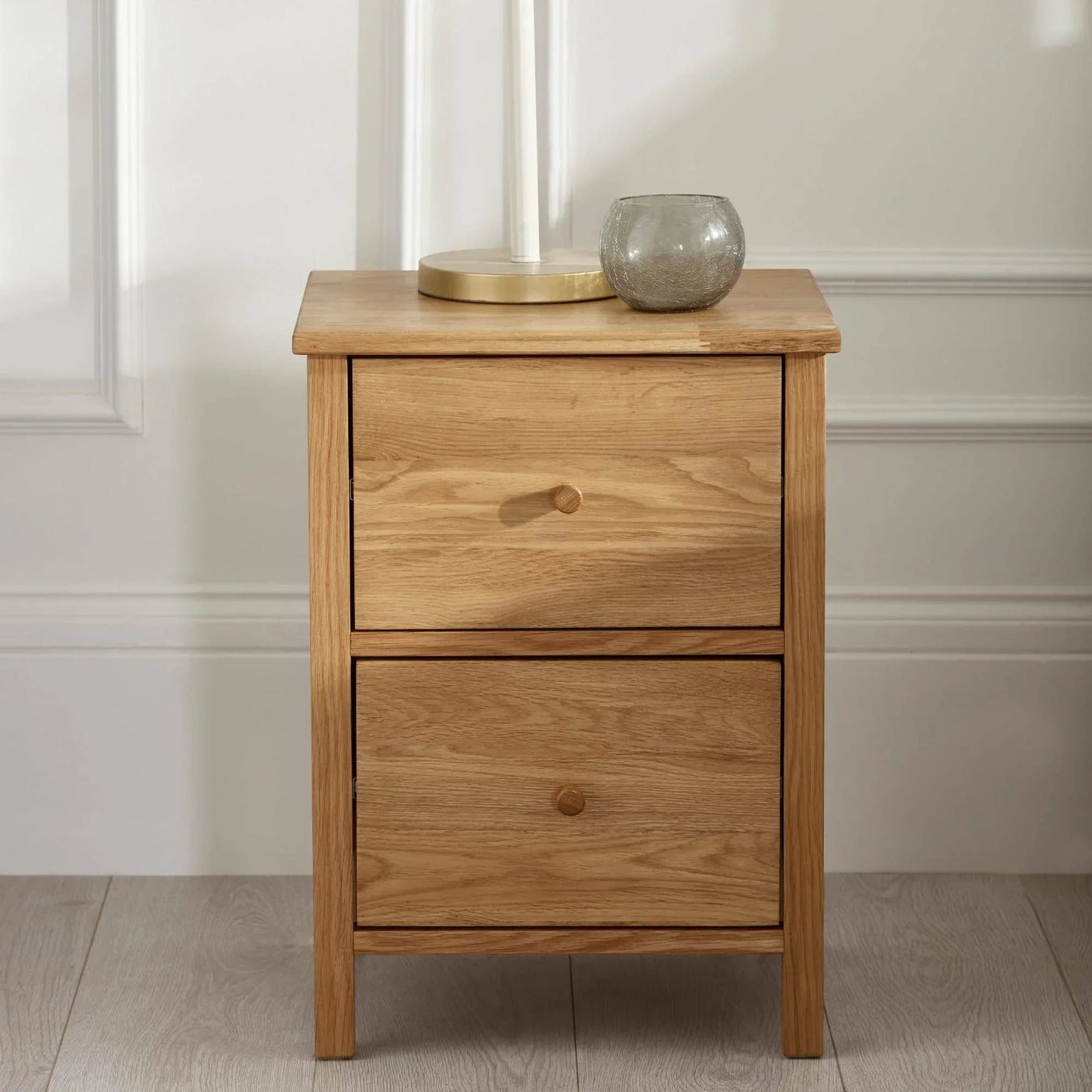 Oak bedside table with two drawers, lamp and glass candle holder on top