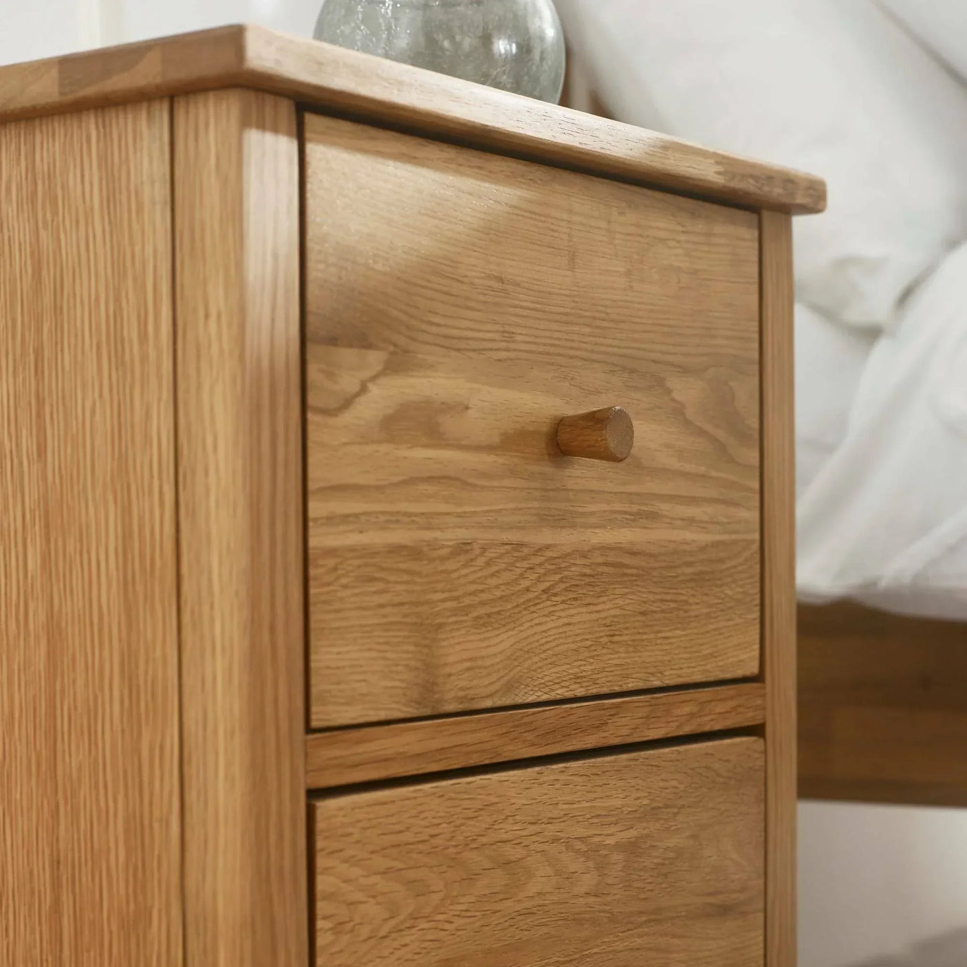 oak bedside table with two drawers and wooden handles beside a bed