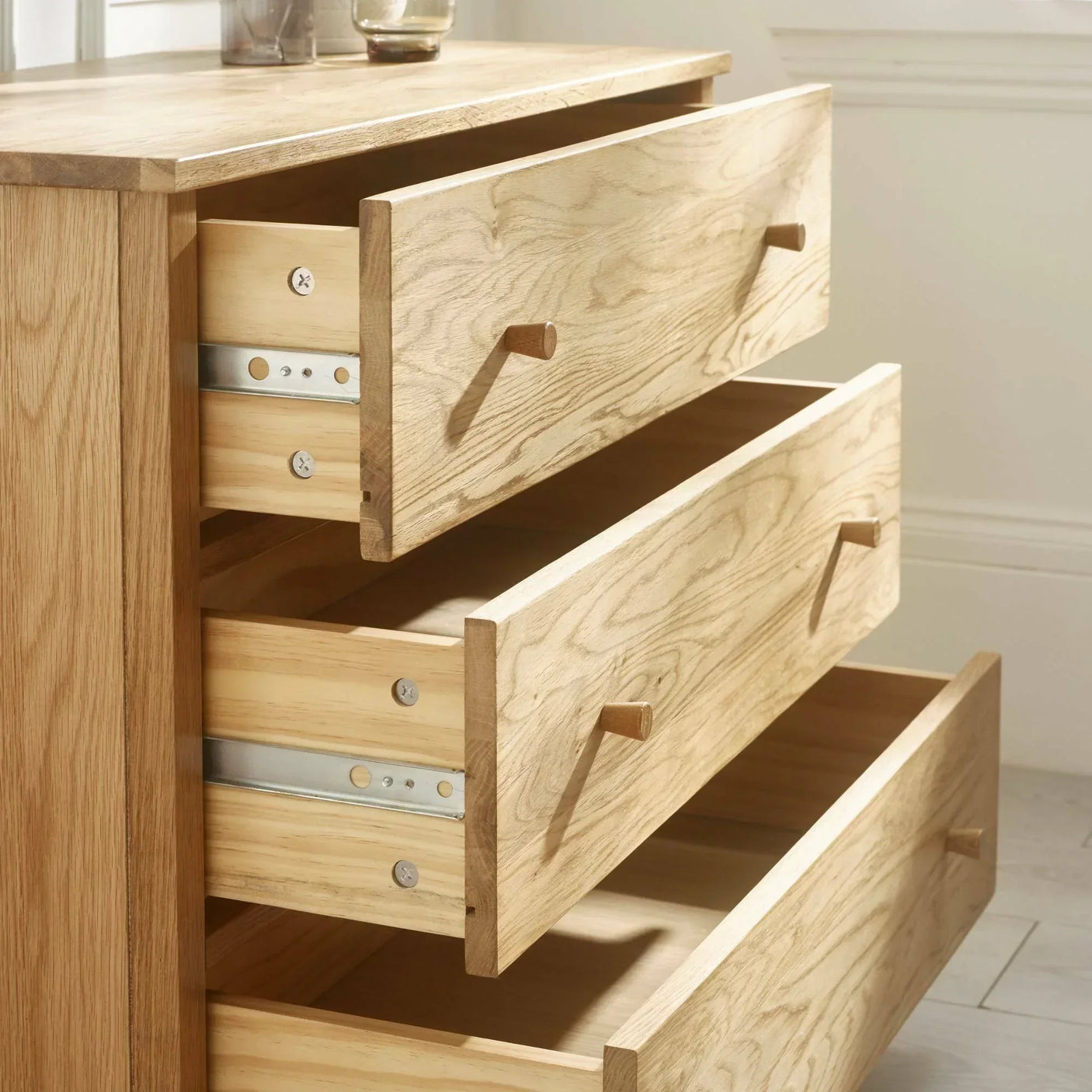 Oak chest of drawers with three open drawers showing wood grain and metal runners