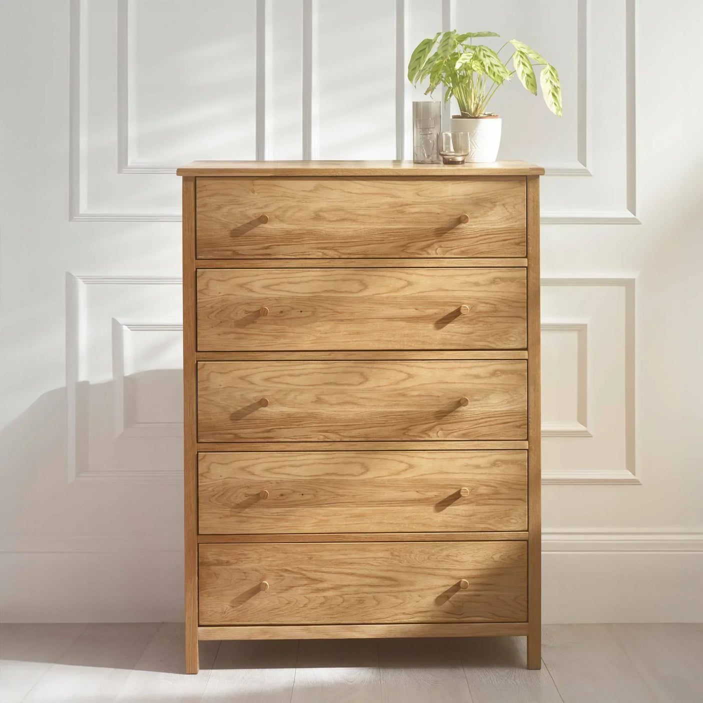 Oak chest of drawers with five drawers and round handles, potted plant on top