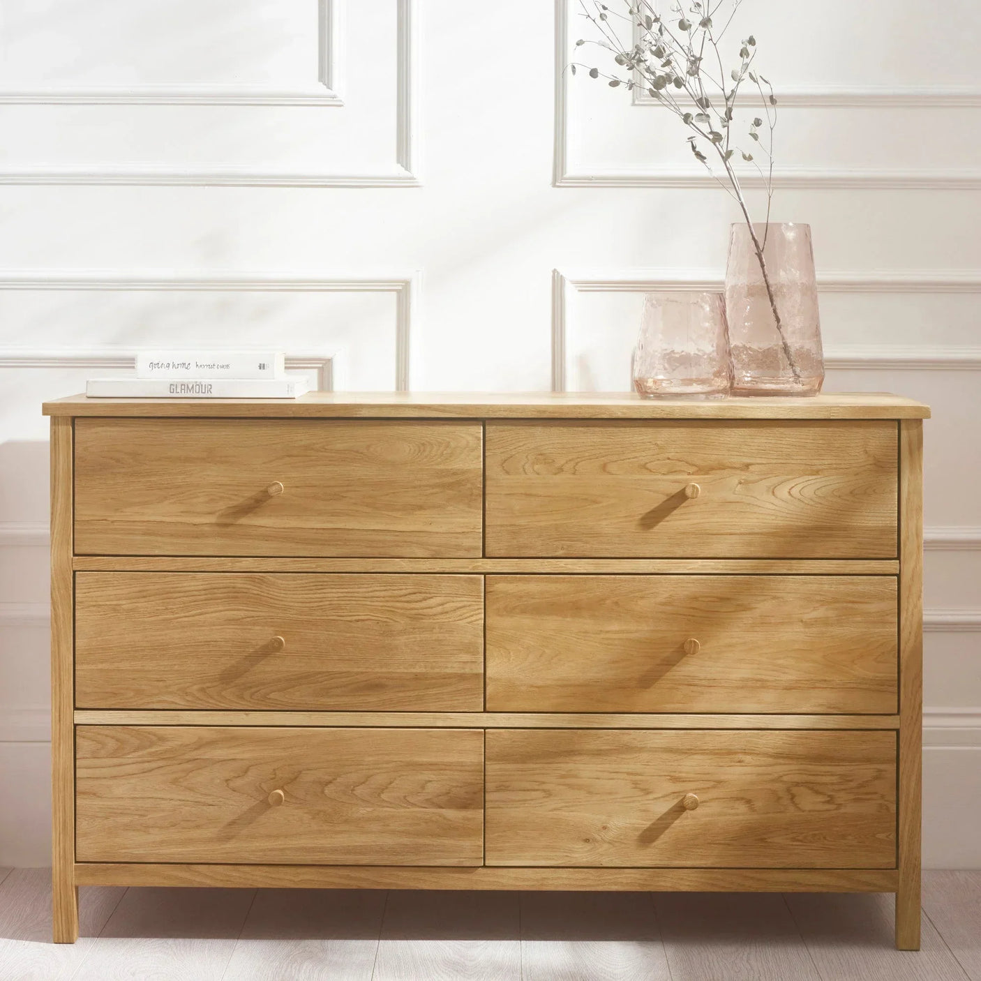 Six drawer oak chest with books and glass vases in a bright modern room