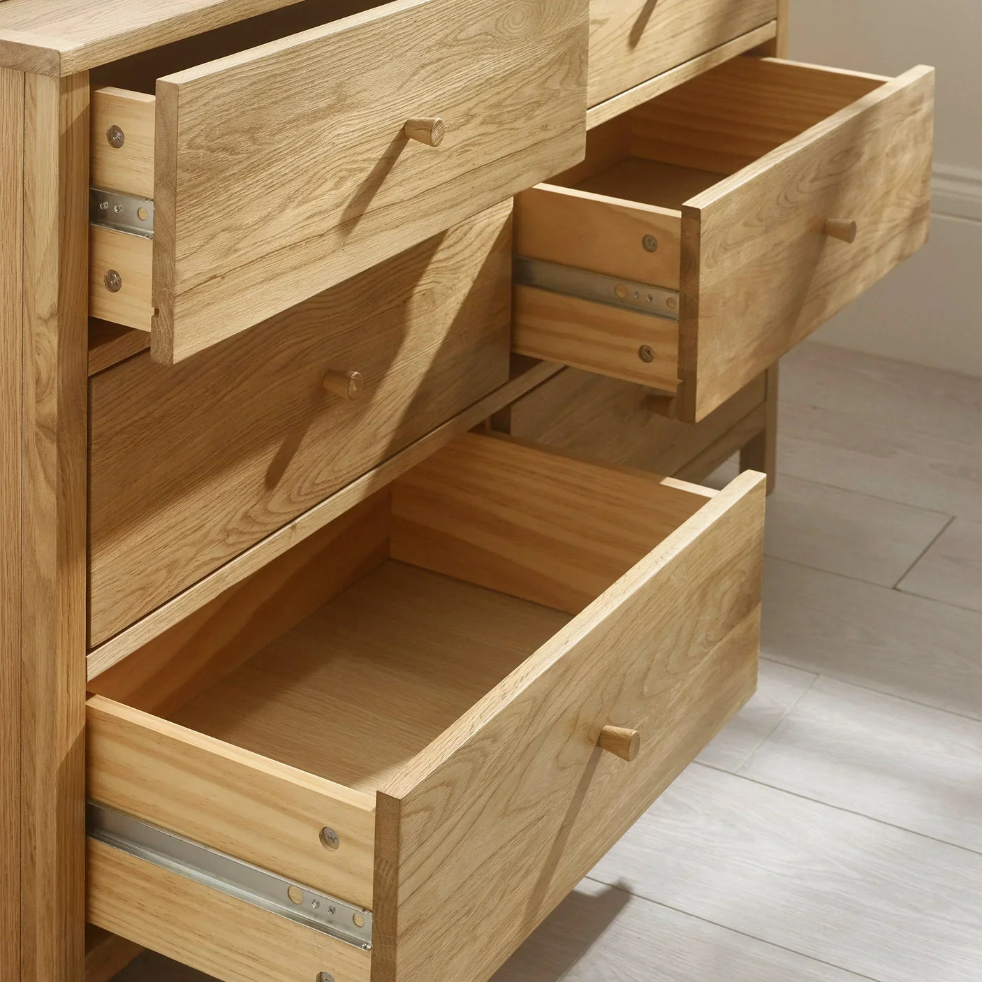 Oak chest of drawers with open drawers on light wood floor
