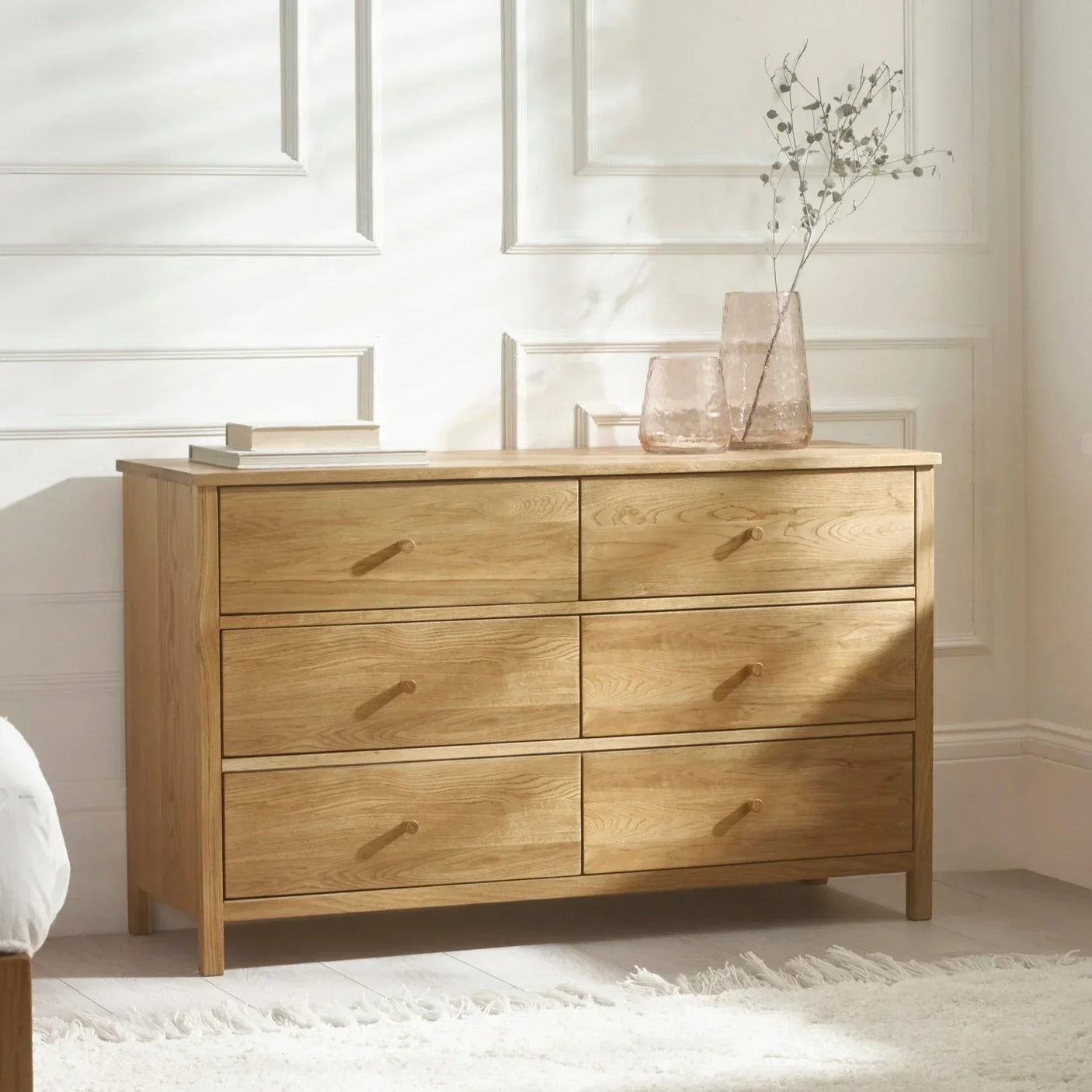 Oak chest of drawers with six drawers in sunlit bedroom, decorative vases on top