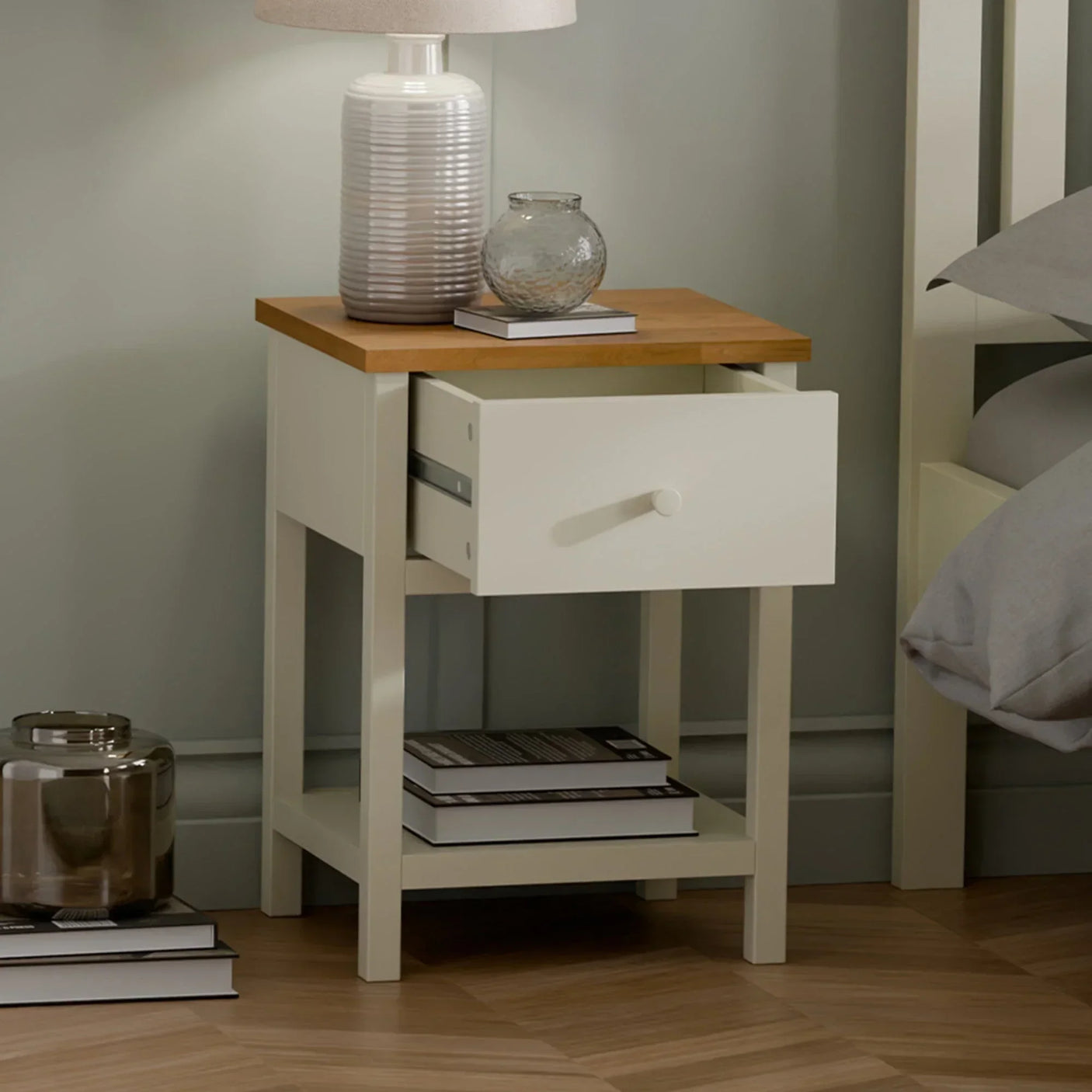 Cream and oak bedside table with open drawer, lamp, glass vase and stacked books