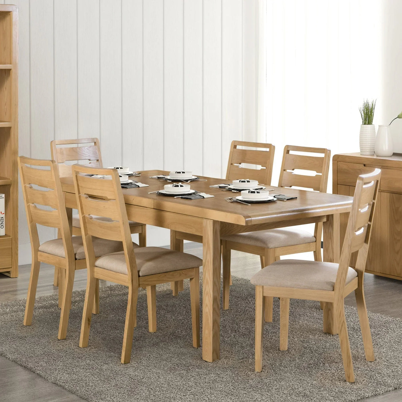 Oak dining table set with six chairs on a grey rug, set for a meal in a modern room