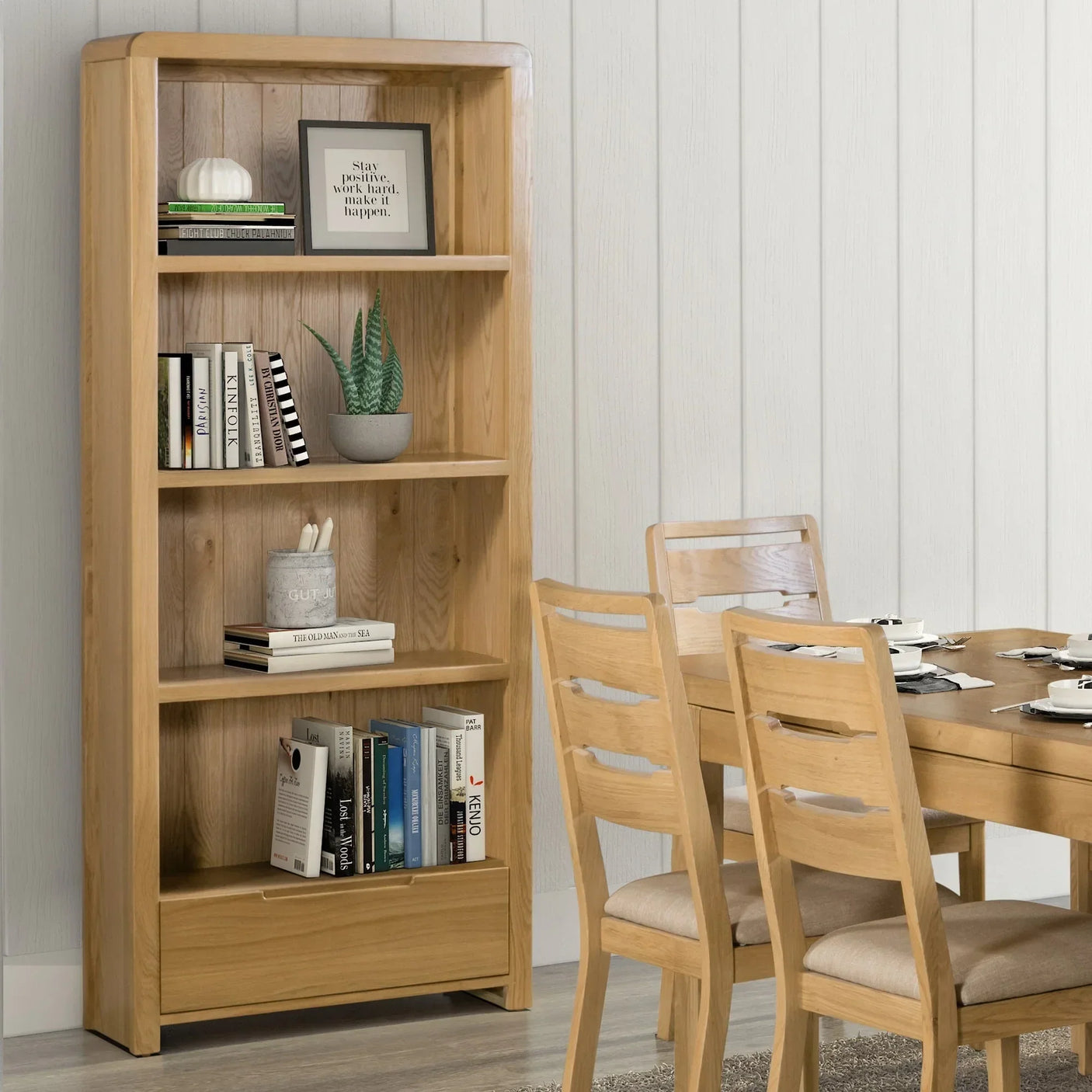 Oak tall bookcase with shelves and drawer beside dining table and chairs in modern room