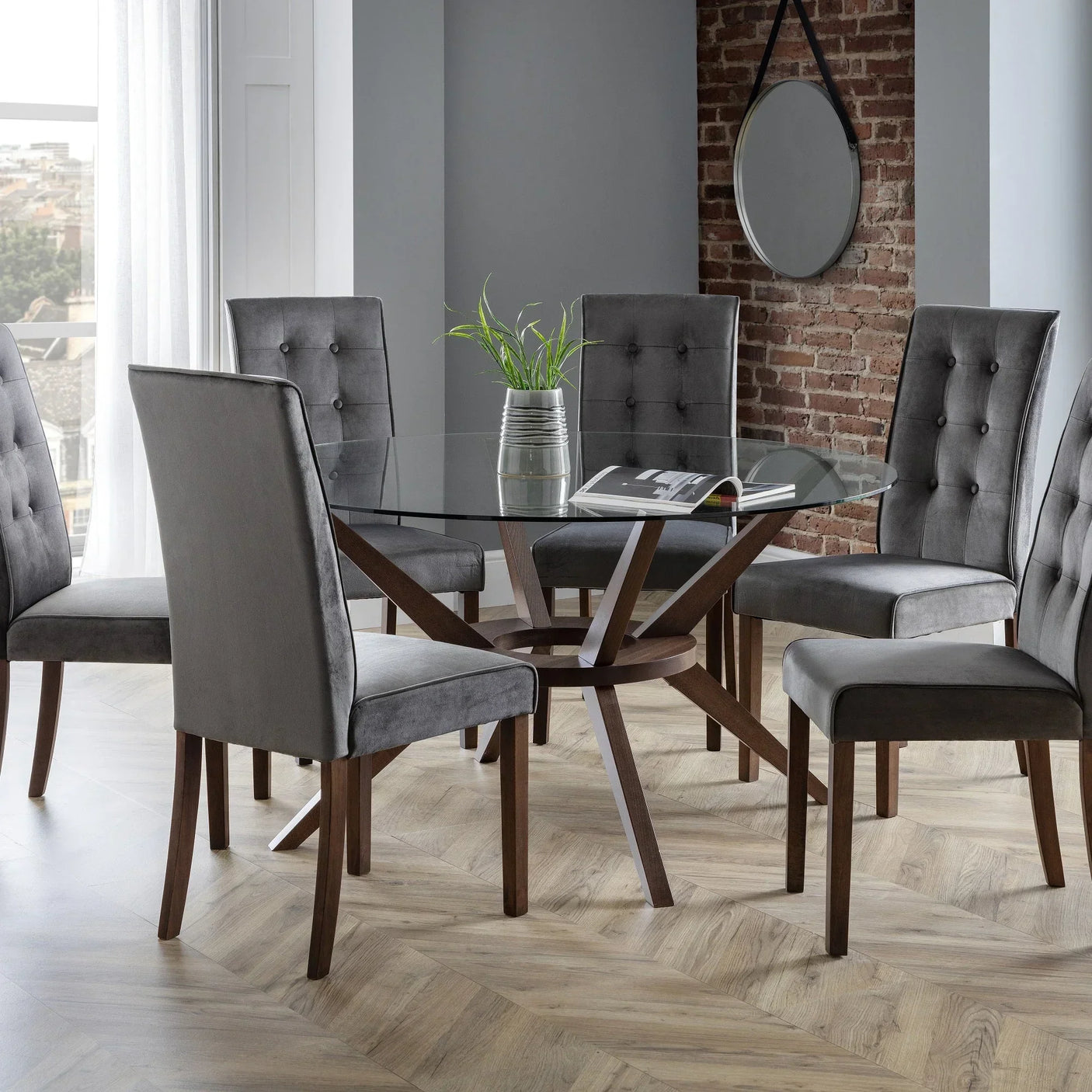 Glass dining table with dark wood base and six grey upholstered chairs in modern room