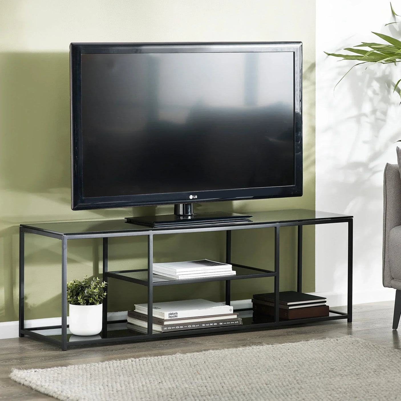 Black metal Chicago TV unit with open shelves holding books and plant, flat screen TV on top