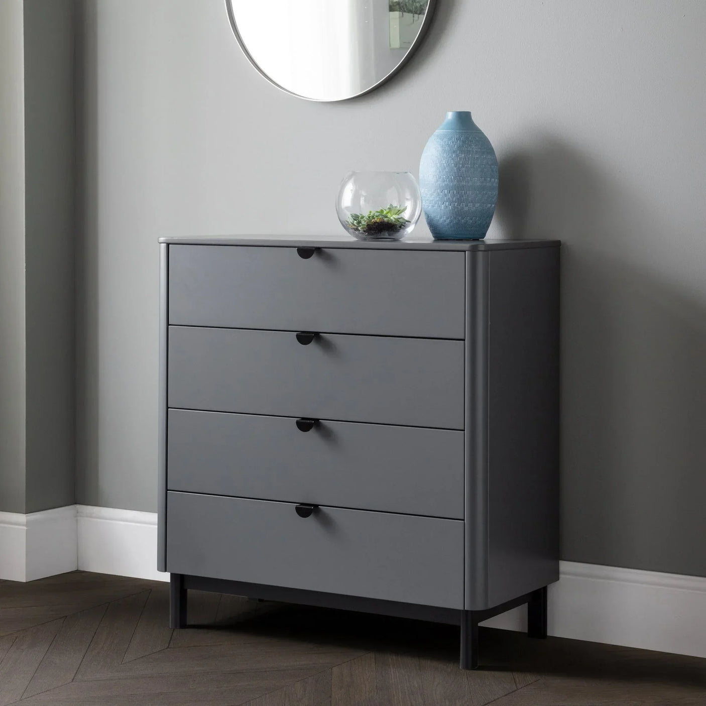 Grey 4 drawer chest with round mirror above, blue vase and glass bowl on top