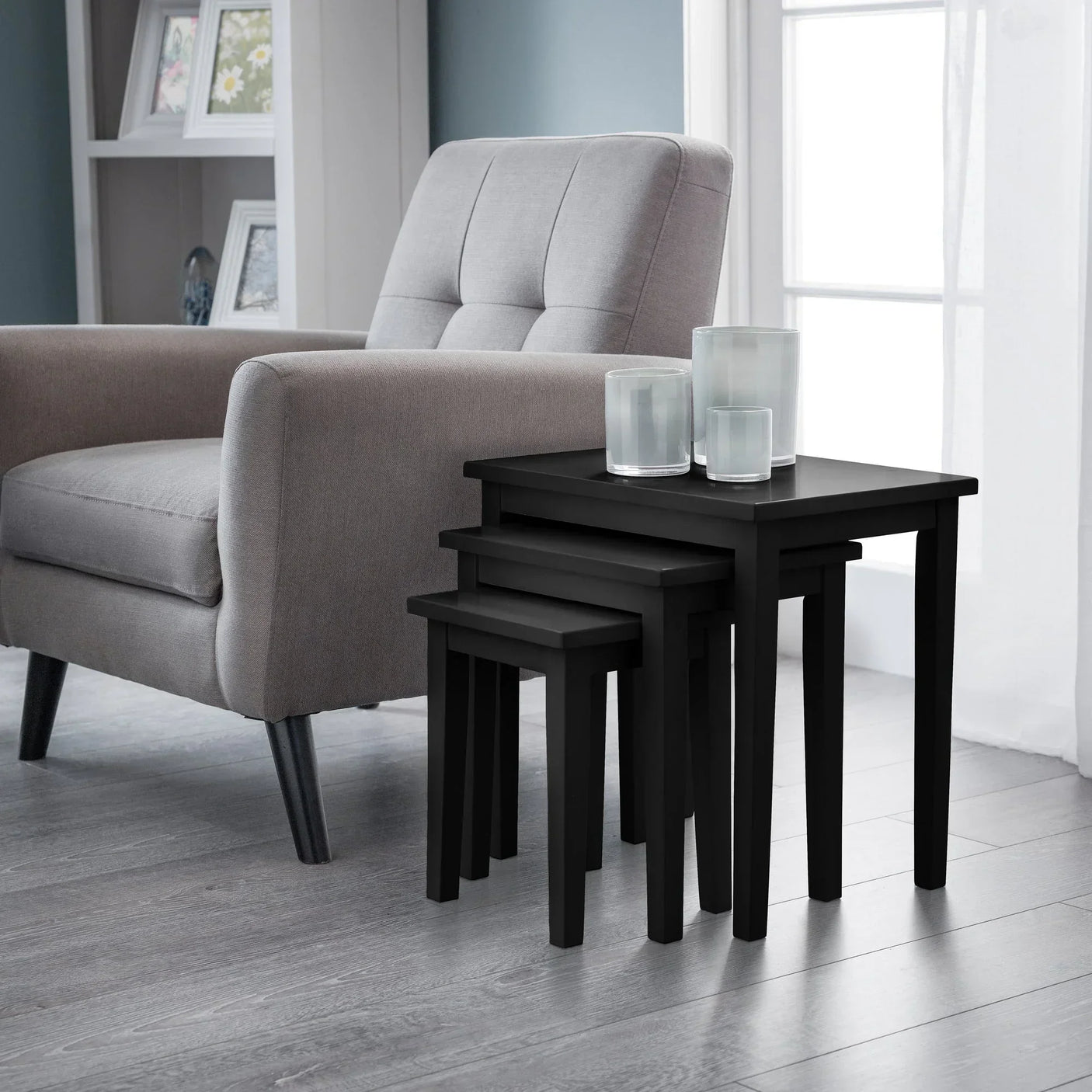 Black nest of tables with glass candle holders beside grey armchair in living room
